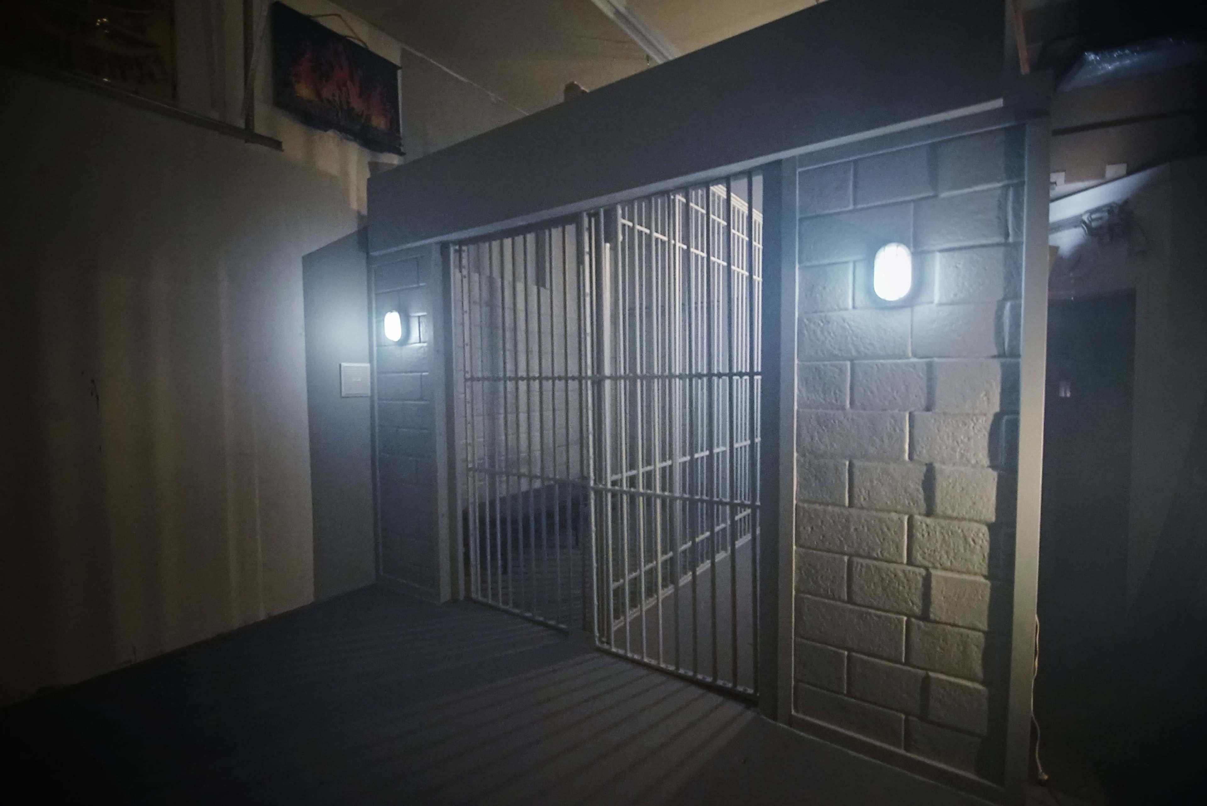 A dimly lit corridor featuring a barred cell door with two mounted lights on either side.