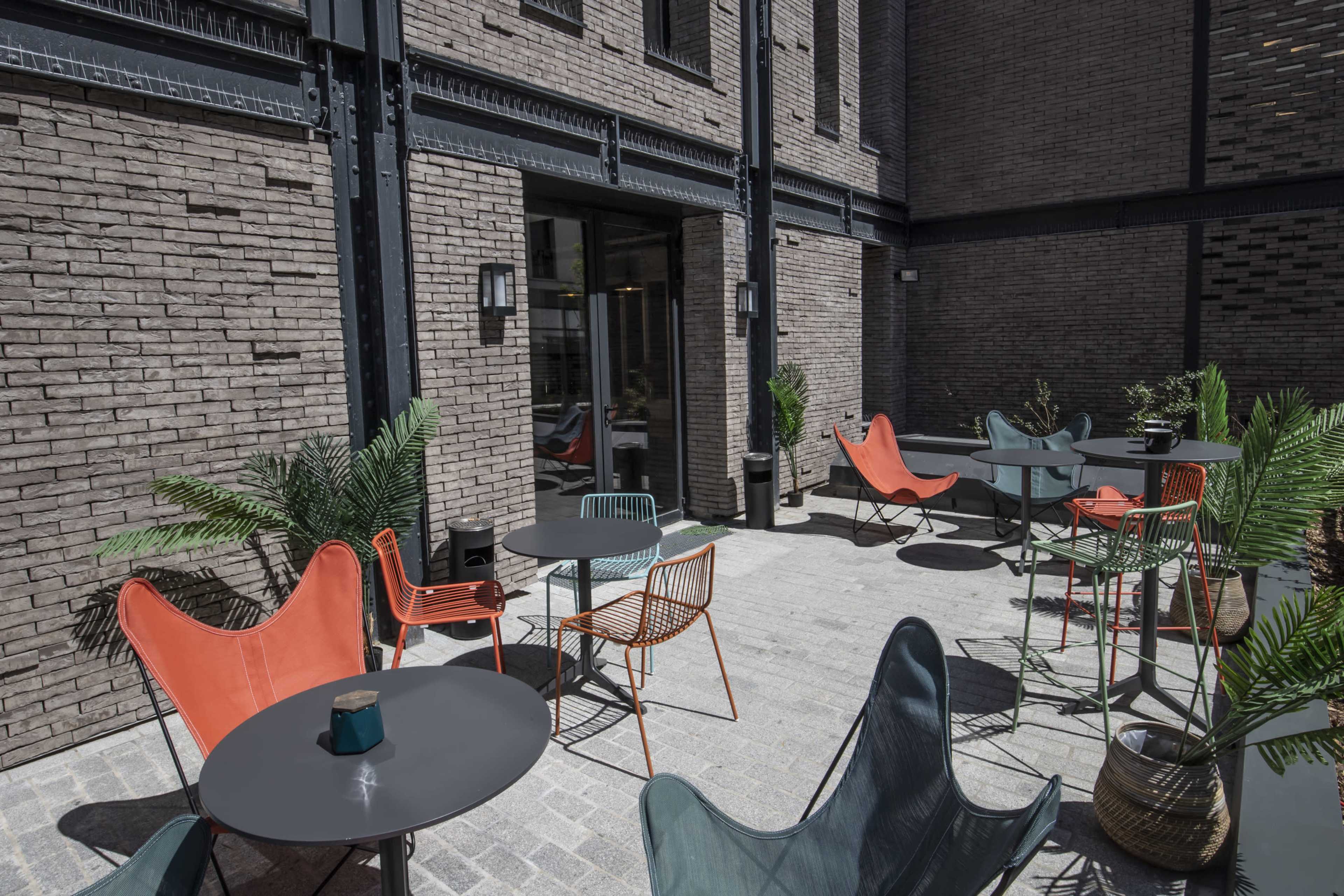 A modern outdoor seating area with various chairs and tables surrounded by brick walls and greenery.
