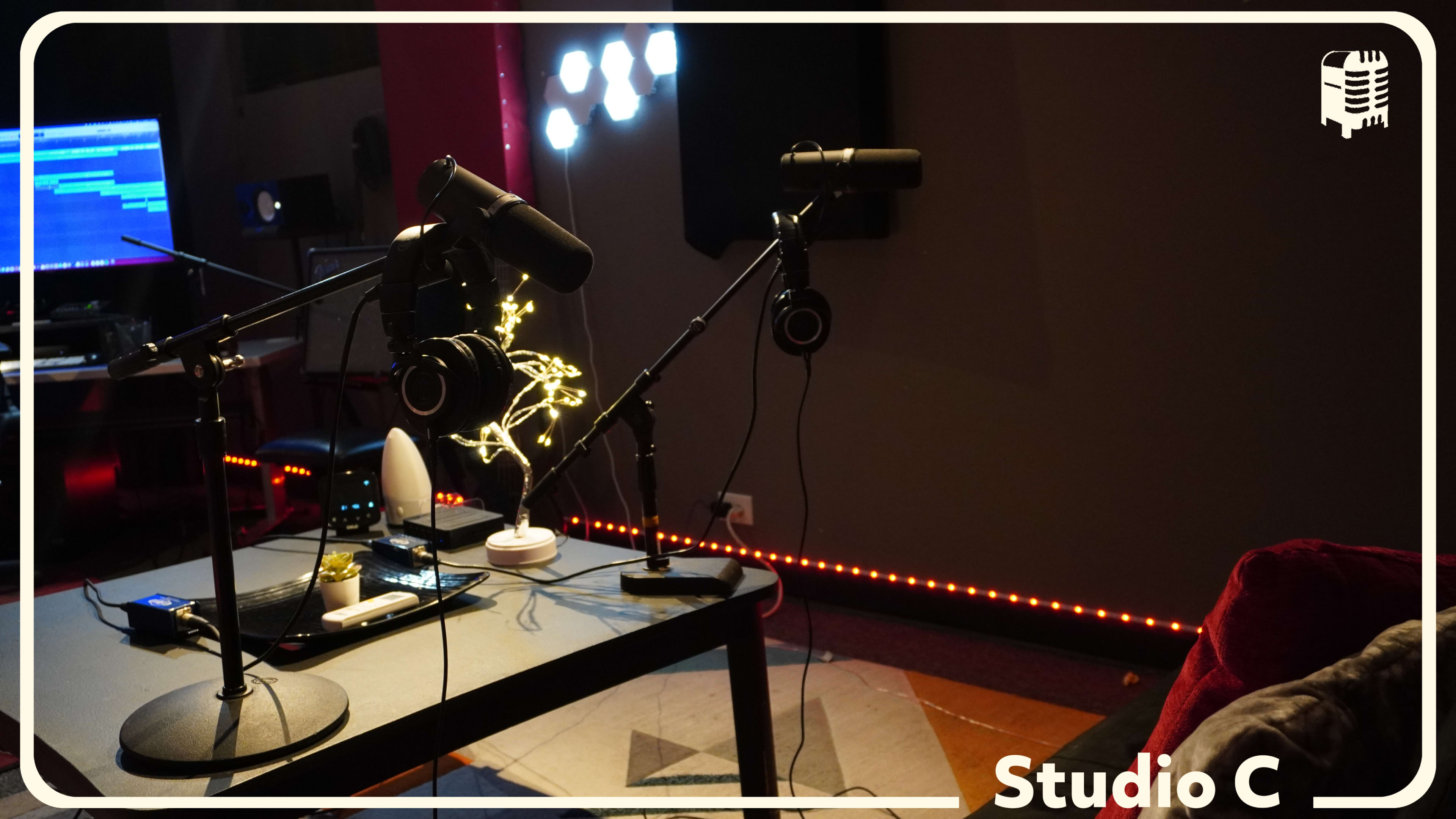The image shows a recording studio with two microphones on stands, headphones, and a computer setup in the background.