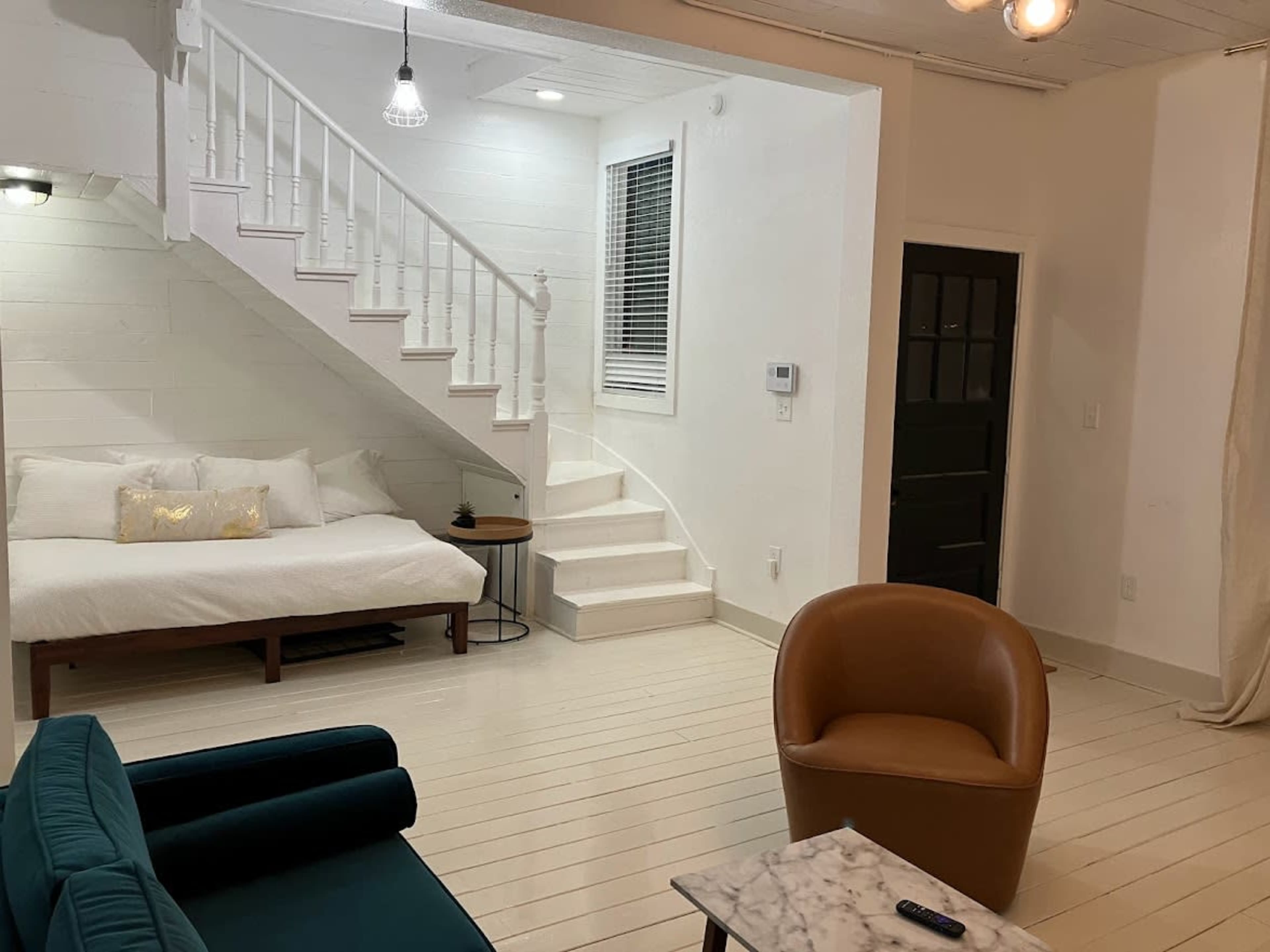 A modern living space with a staircase, a couch, a coffee table, and a bed positioned along one wall.