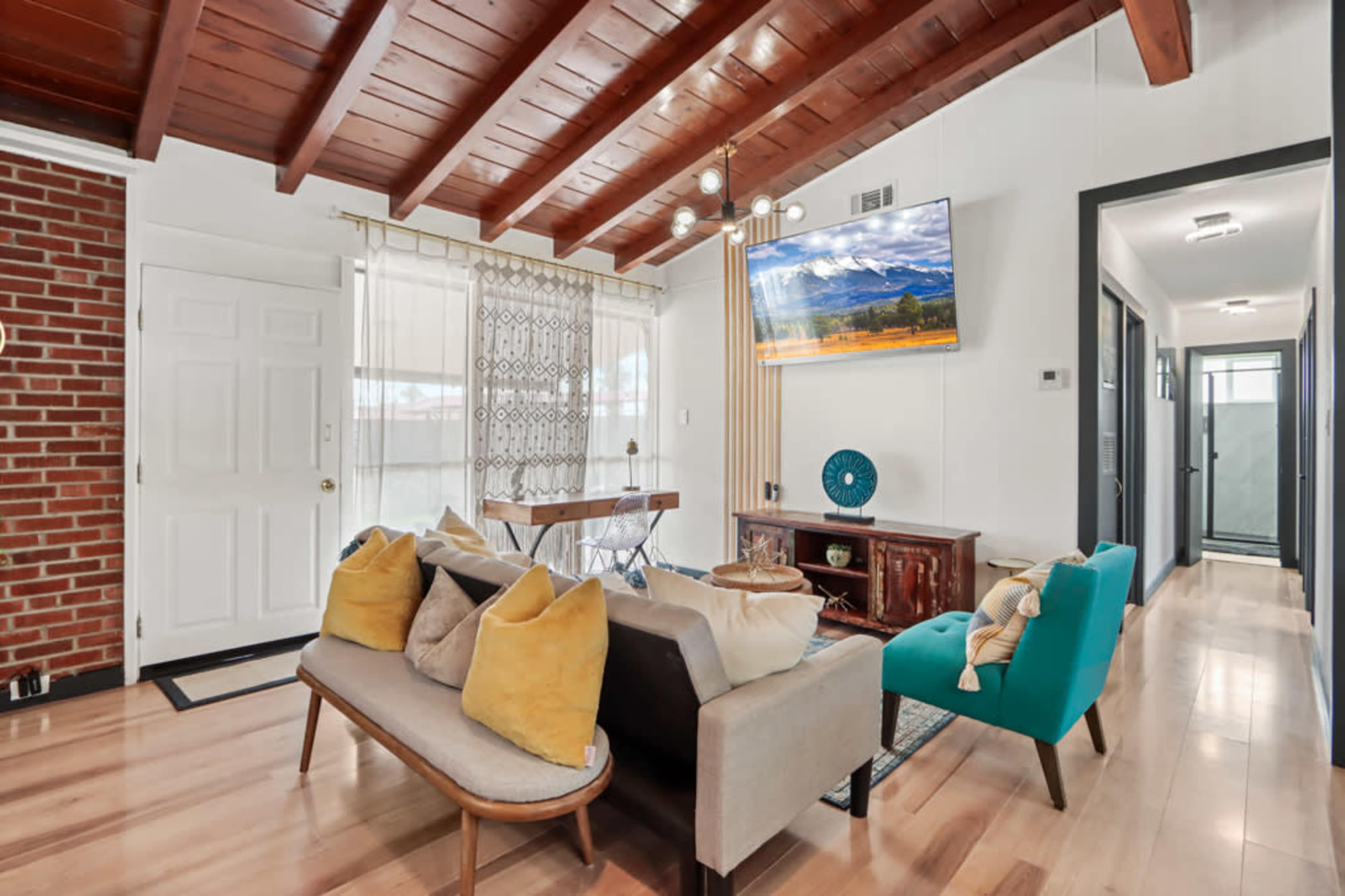 The living room features wooden ceiling beams, a large television mounted on the wall, and a mix of modern and vintage furniture.