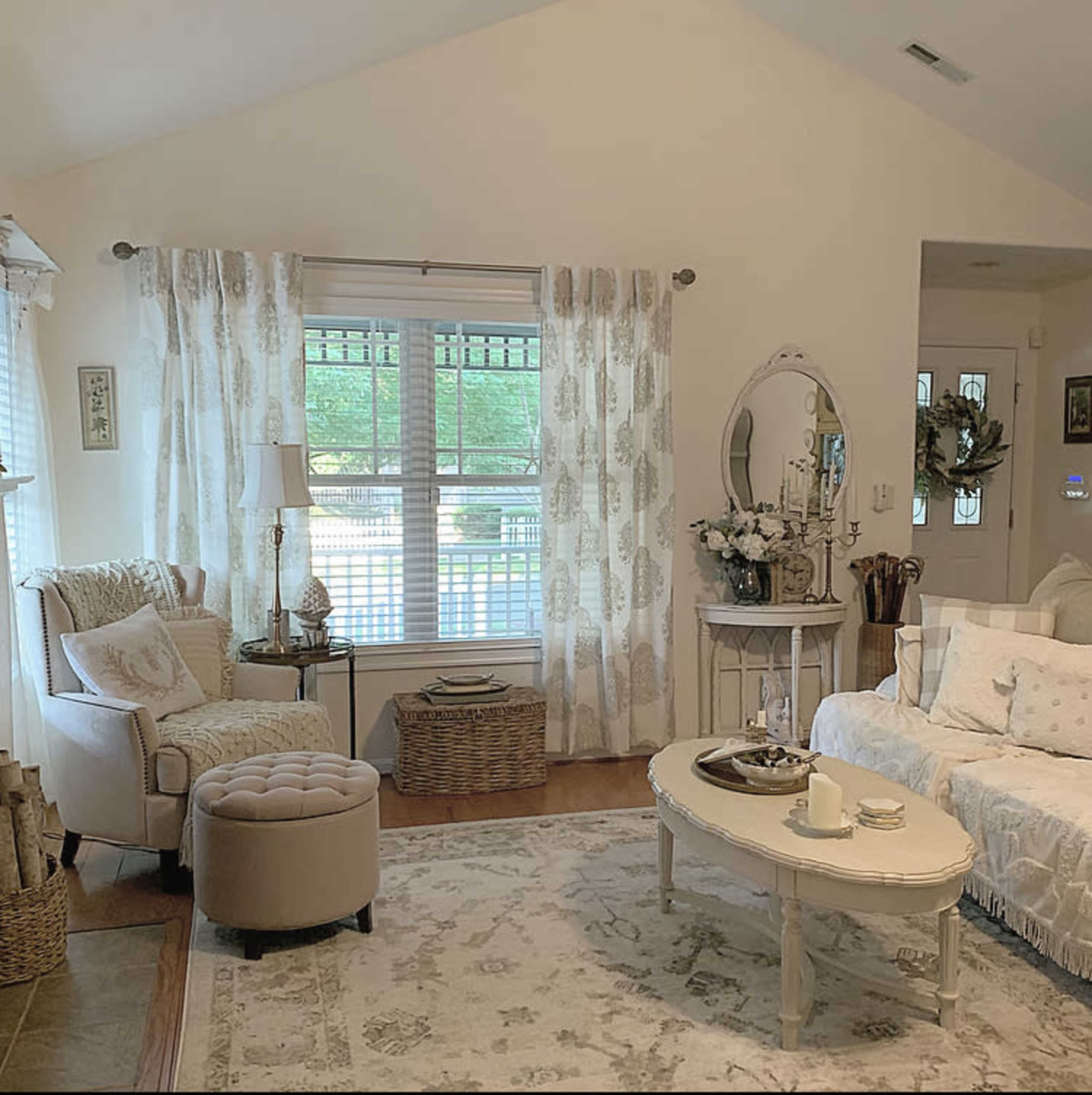 A cozy living room with a light-colored sofa, a round coffee table, and a sitting area near a window dressed with sheer curtains.