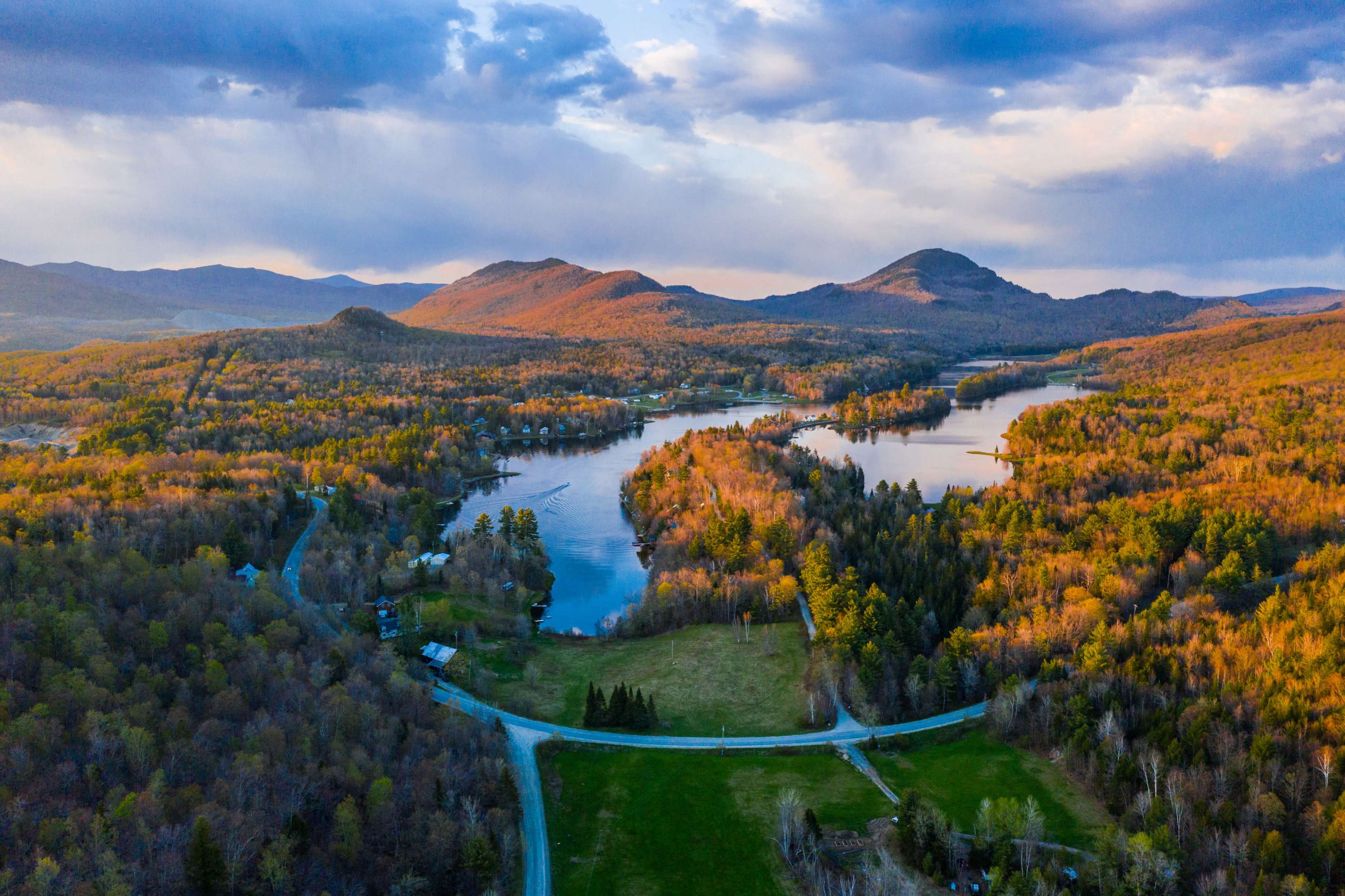 A scenic aerial view of a valley with a winding river surrounded by forested hills and mountains during sunset.
