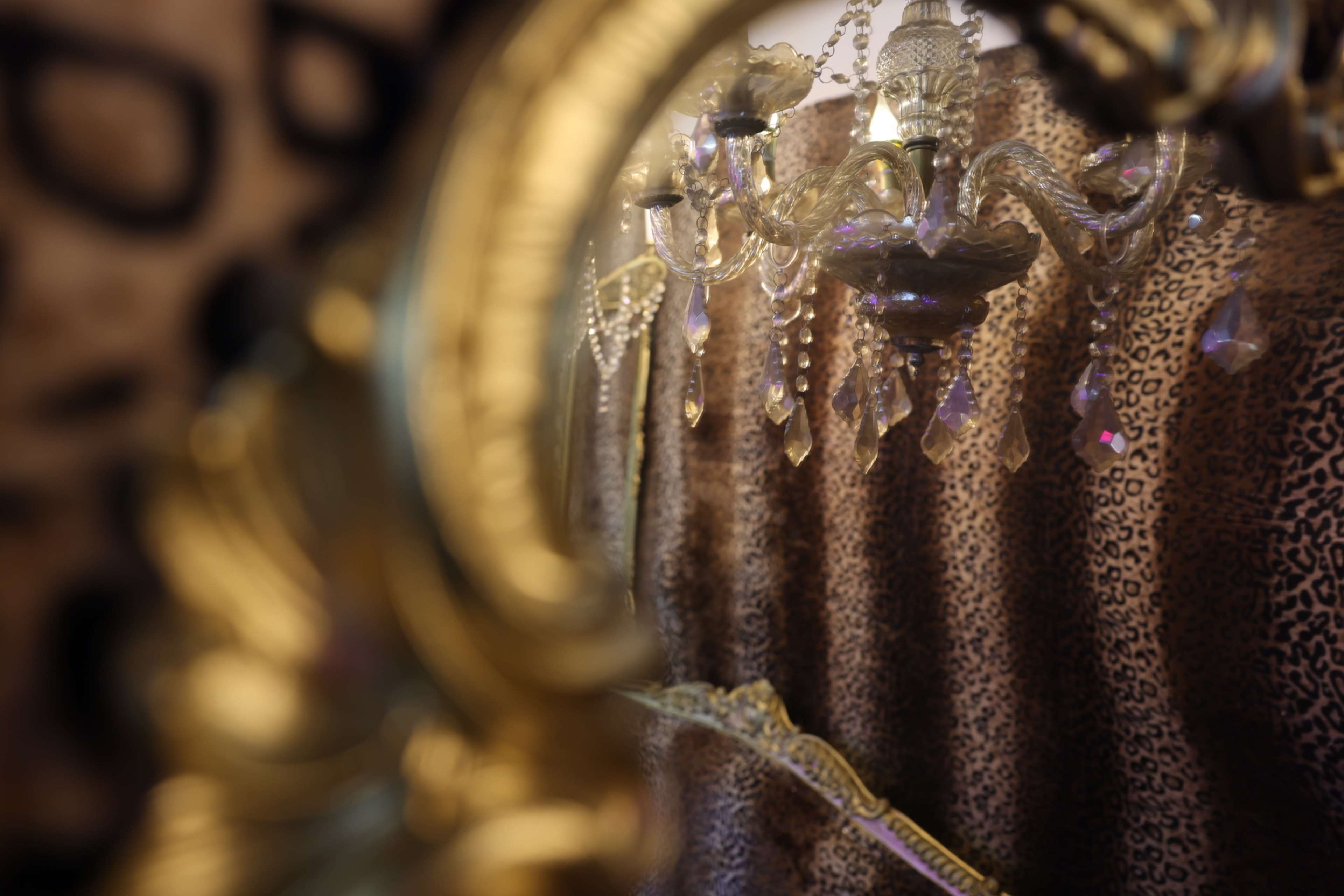 The image shows a chandelier with crystal accents reflected in a decorative mirror, set against a backdrop of leopard-print curtains.