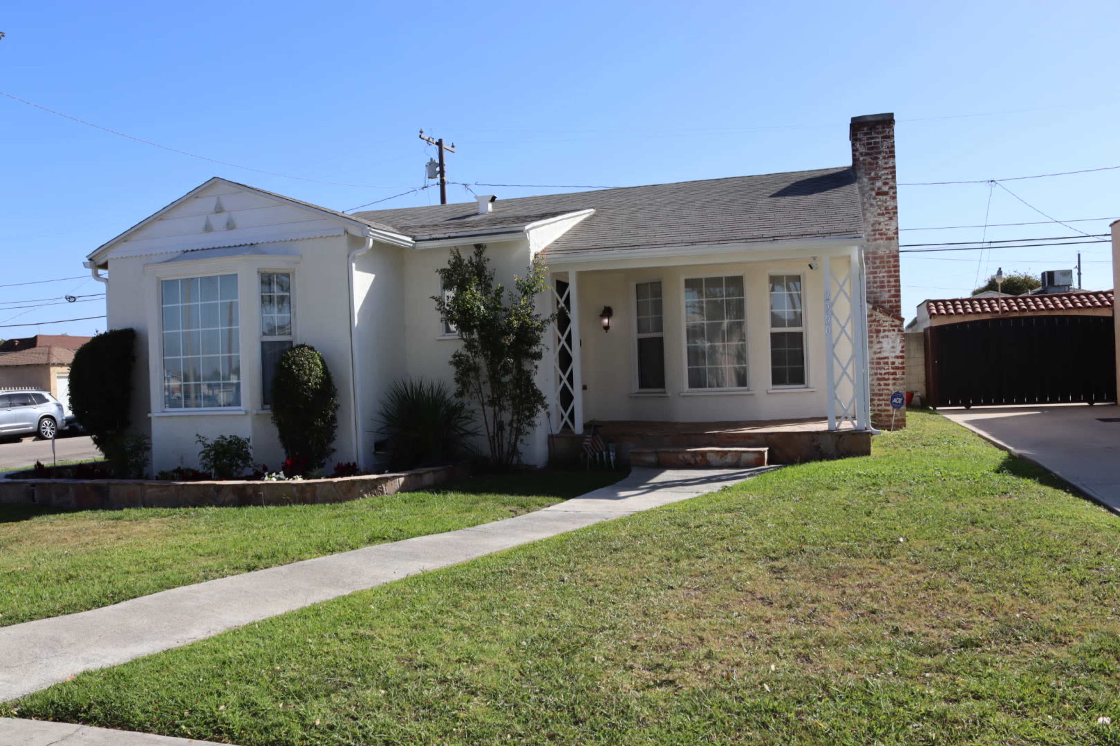 A single-story white house with a sloped roof, a front walkway, and a green lawn.