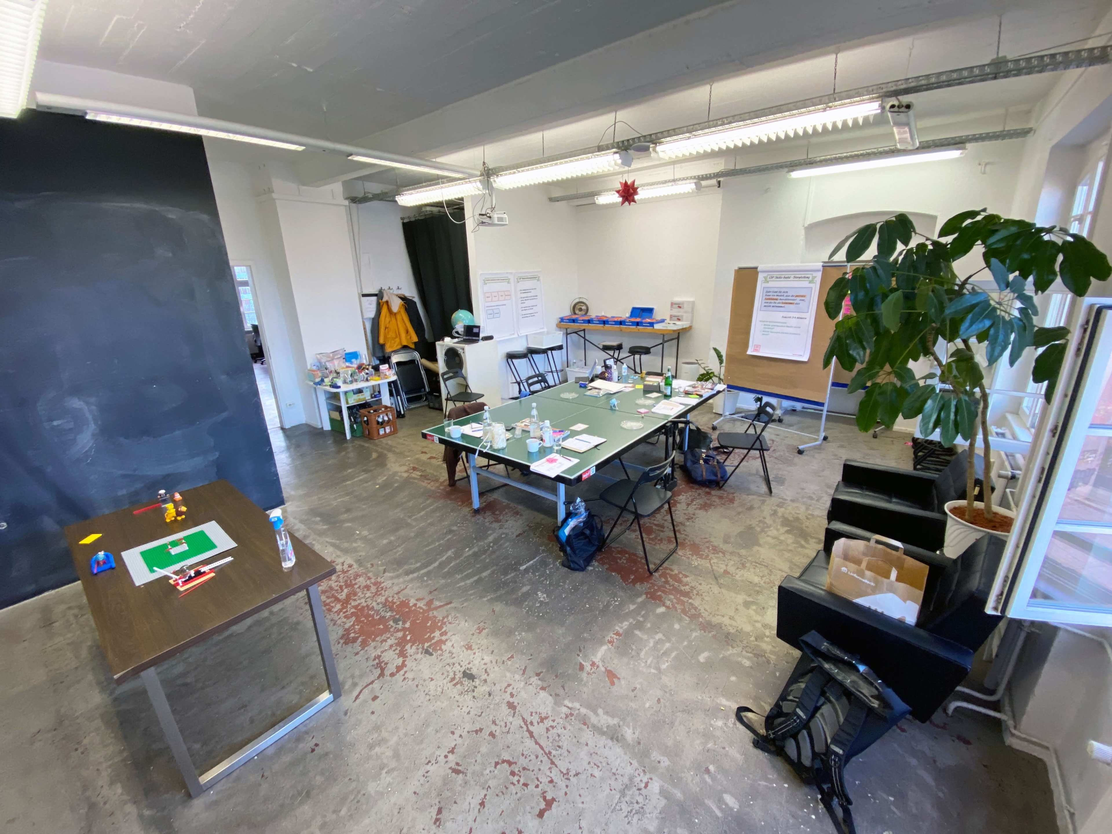 A spacious, well-lit office setting with several tables arranged for a meeting, chairs, and a large green plant in the corner.