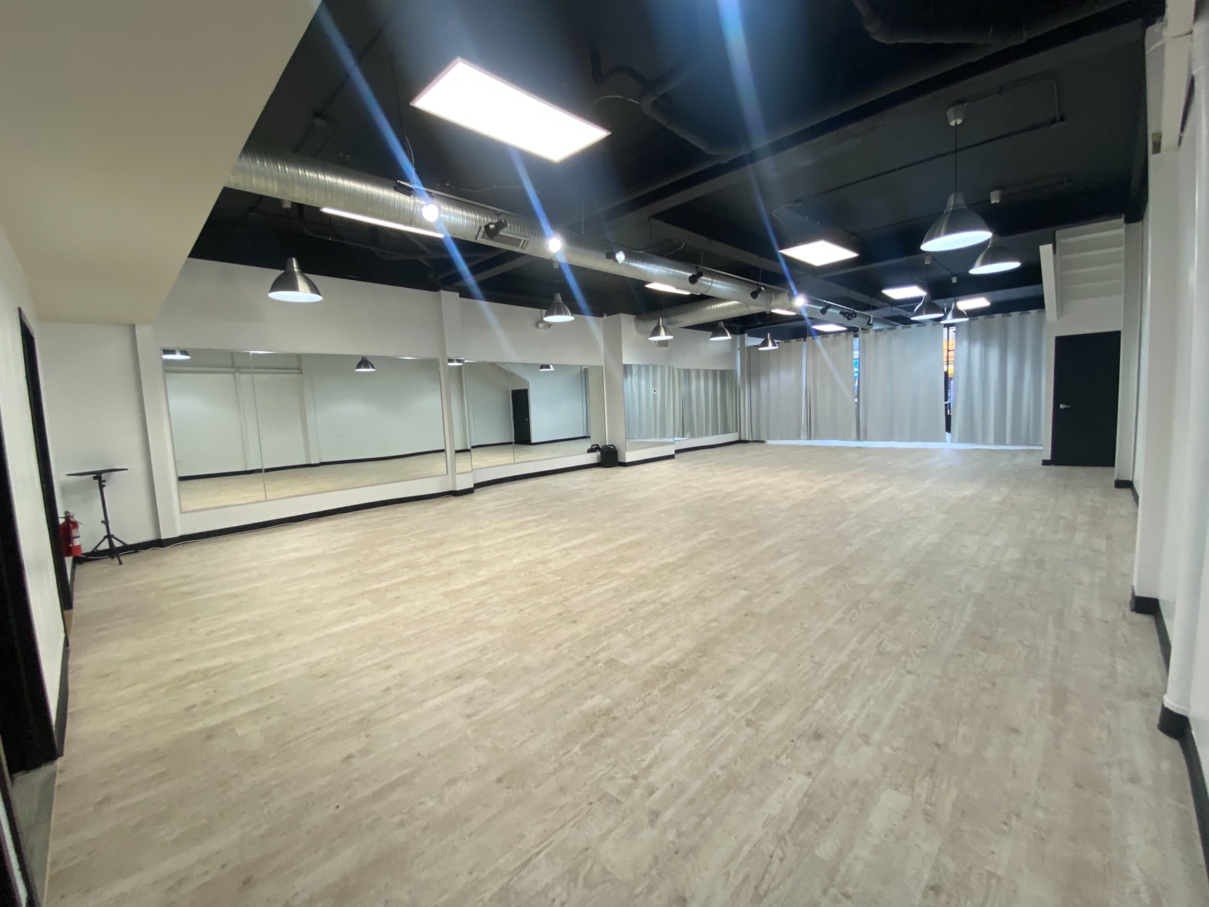 A spacious studio with a light wooden floor, mirrored walls, and overhead lights.