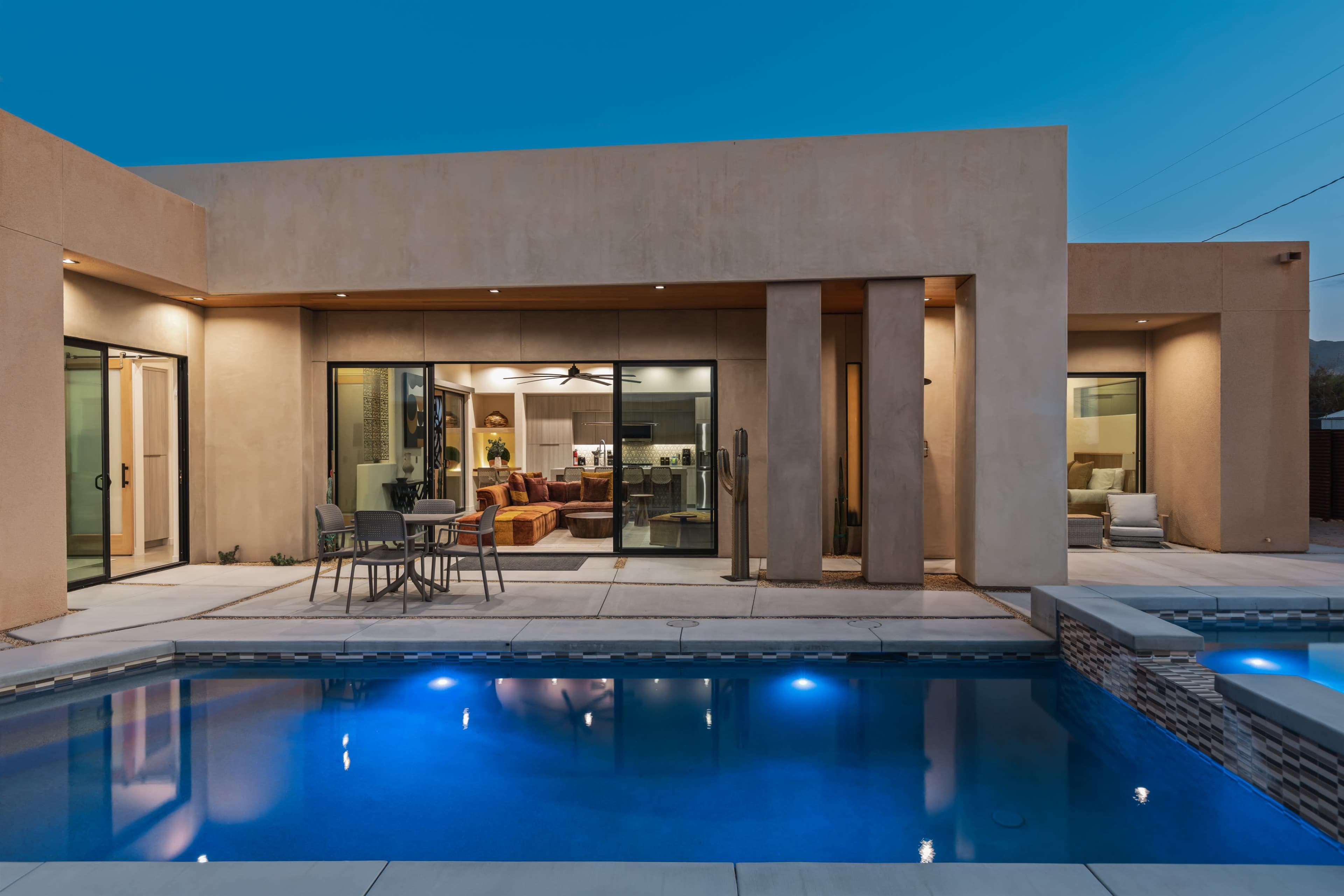 A modern home with large glass doors opens to a patio and pool area, showcasing a sleek design and contemporary furnishings.