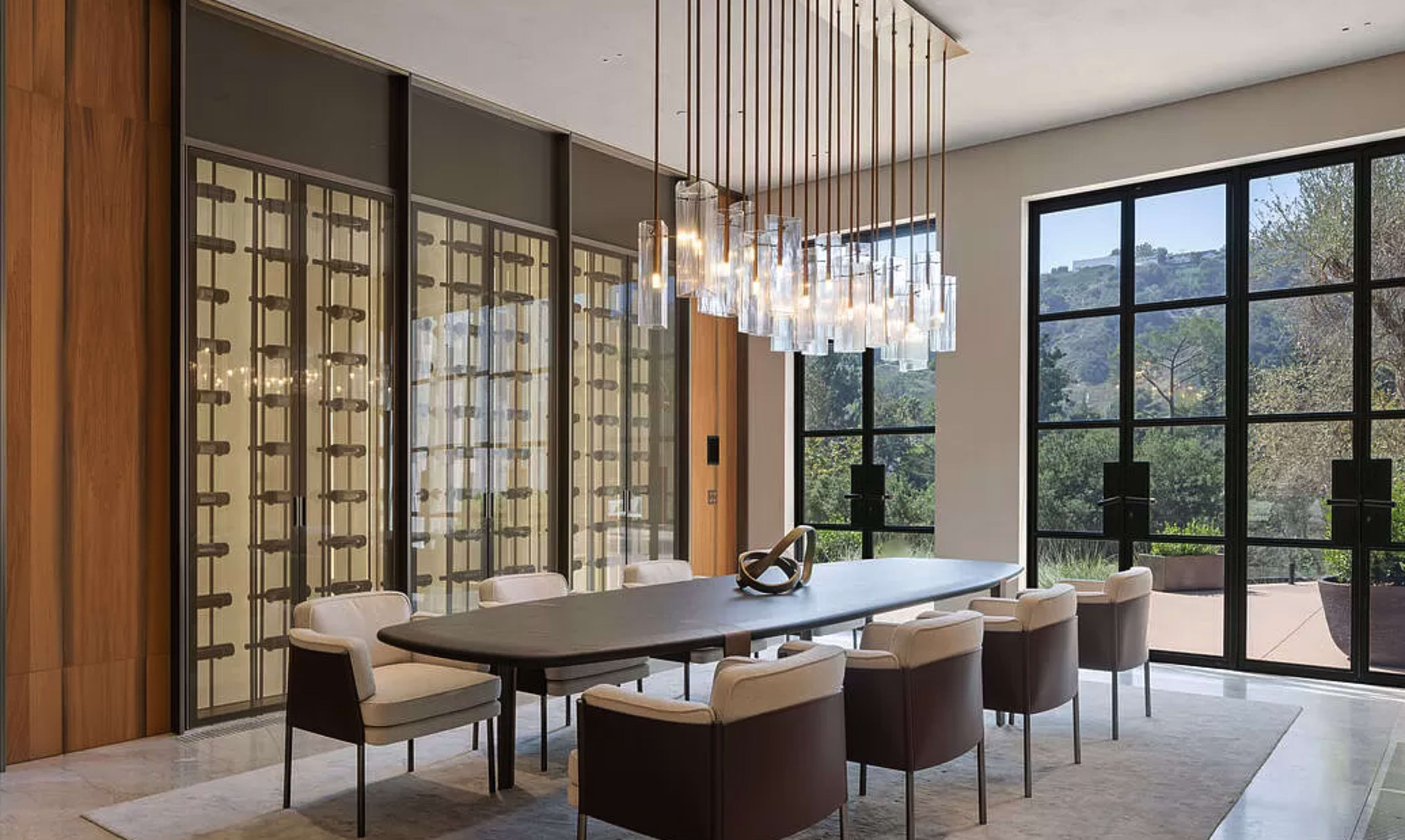 A spacious dining room features a long table surrounded by upholstered chairs and a large, modern light fixture overhead.