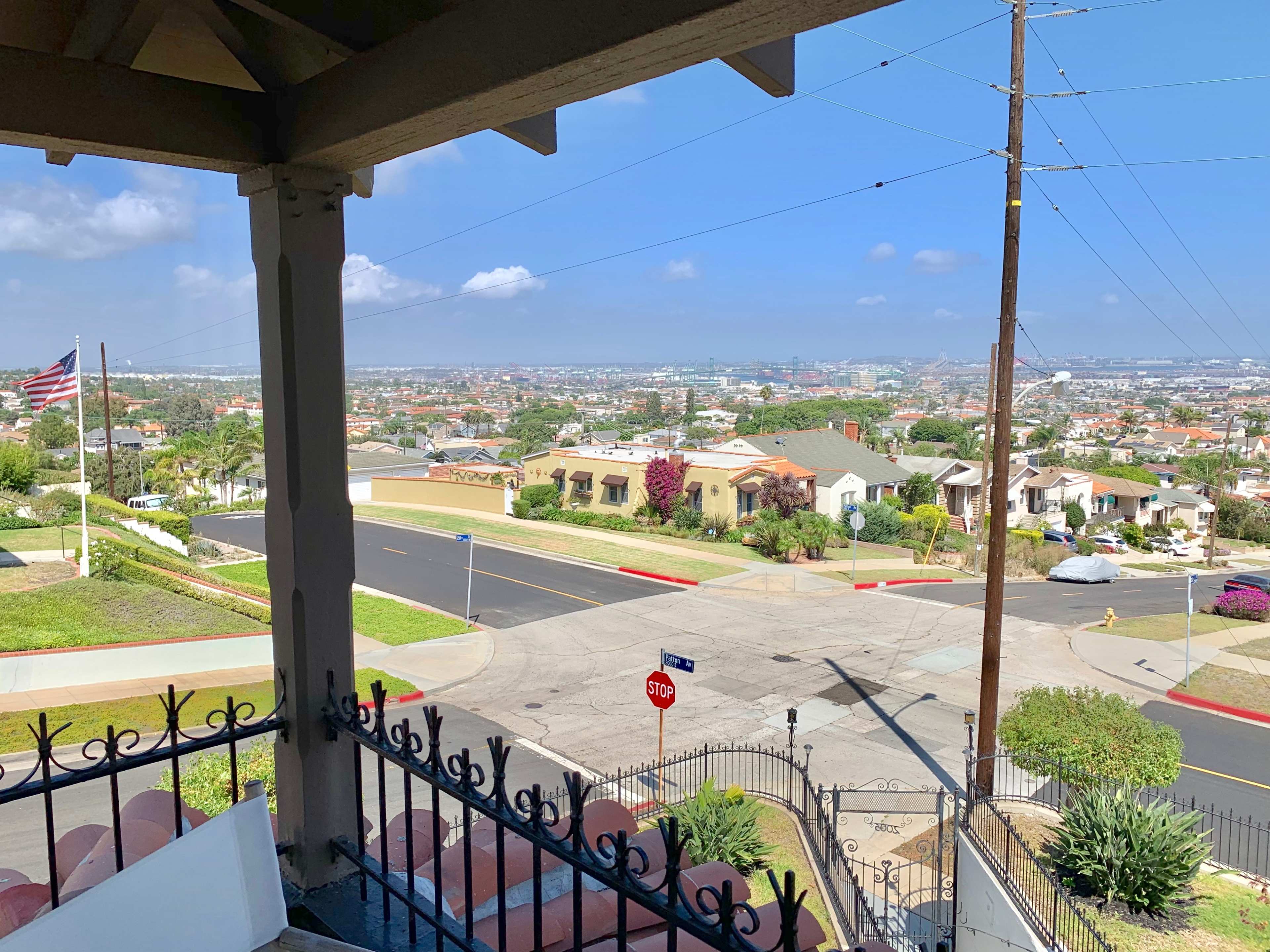 The image shows a view from a porch overlooking a suburban neighborhood with a distant cityscape, power lines, and a stop sign at the intersection below.