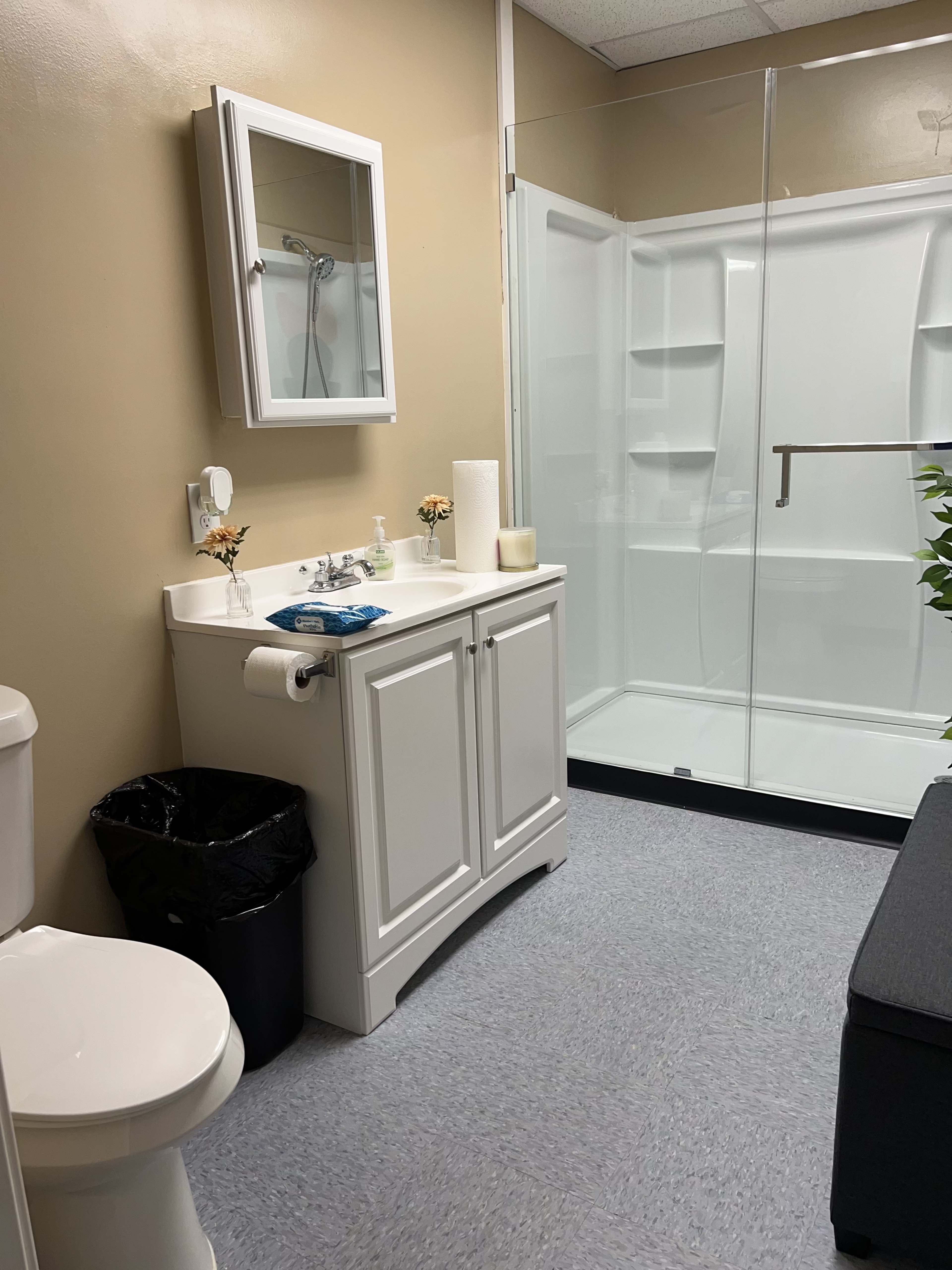 A bathroom with a toilet, a sink cabinet with a mirror above, and a glass-enclosed shower.