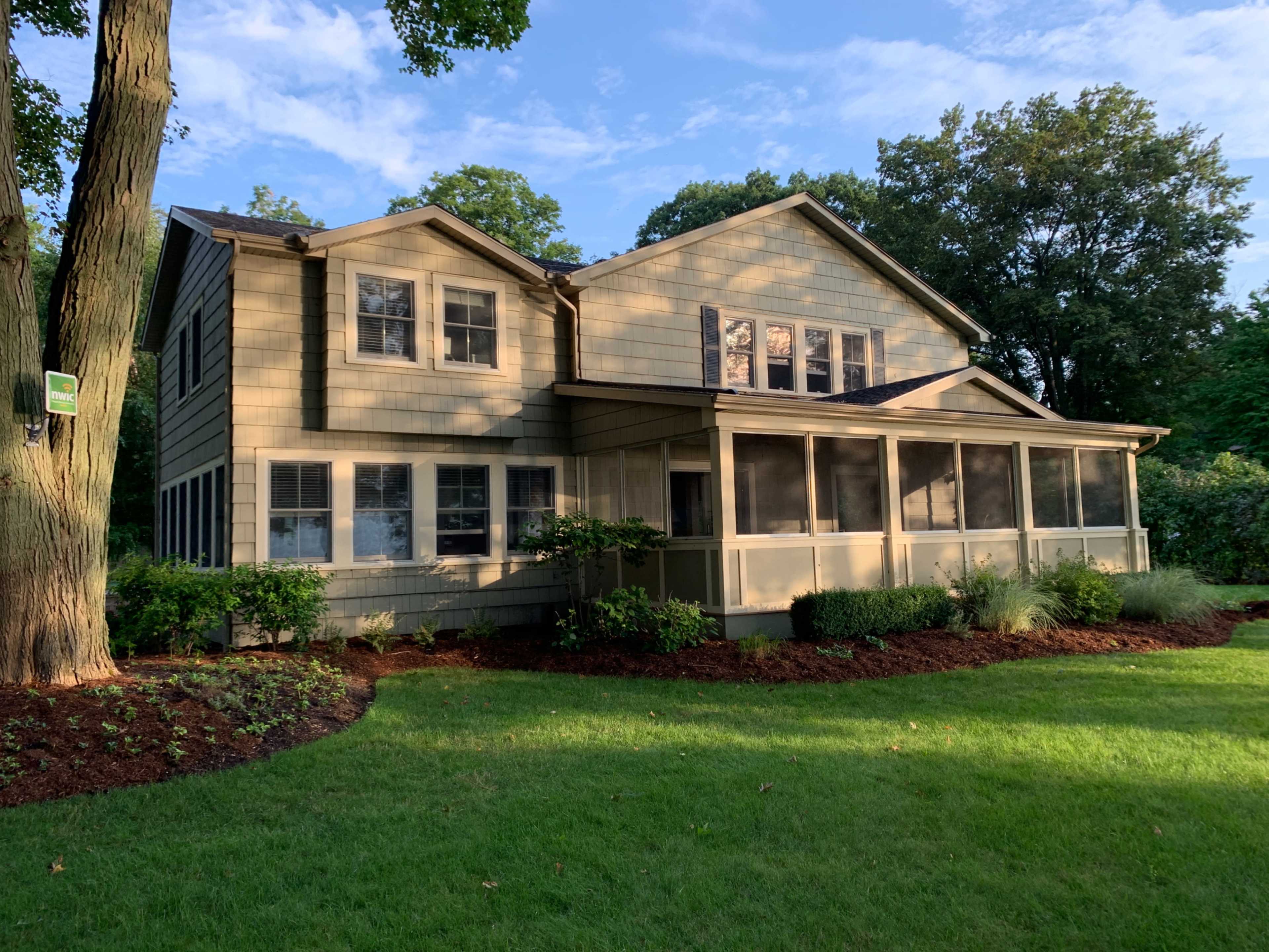 A two-story house with a screened porch, surrounded by a well-maintained lawn and trees.