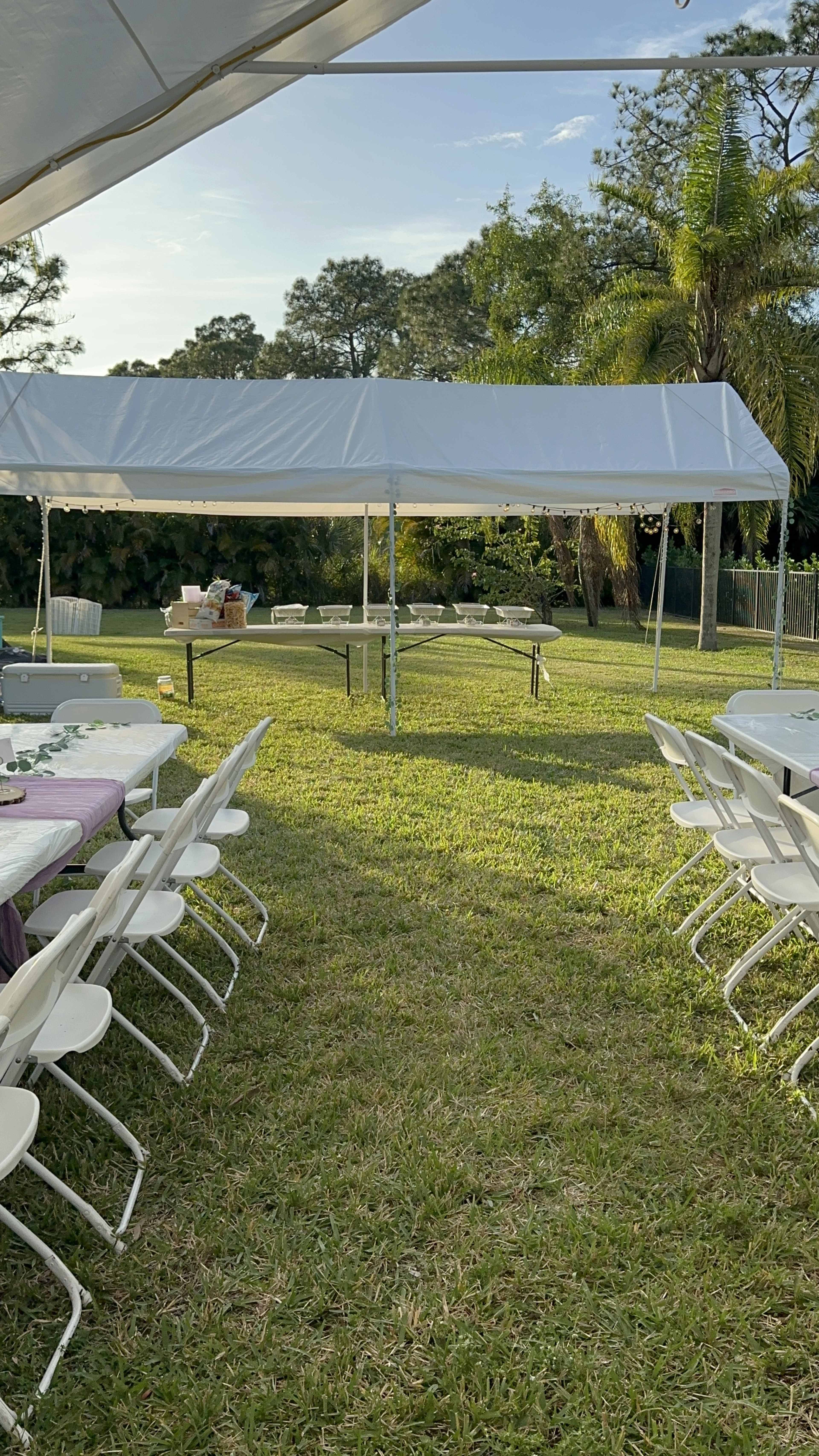 A large white tent is set up on grass, surrounded by rows of folding chairs and tables ready for an outdoor event.
