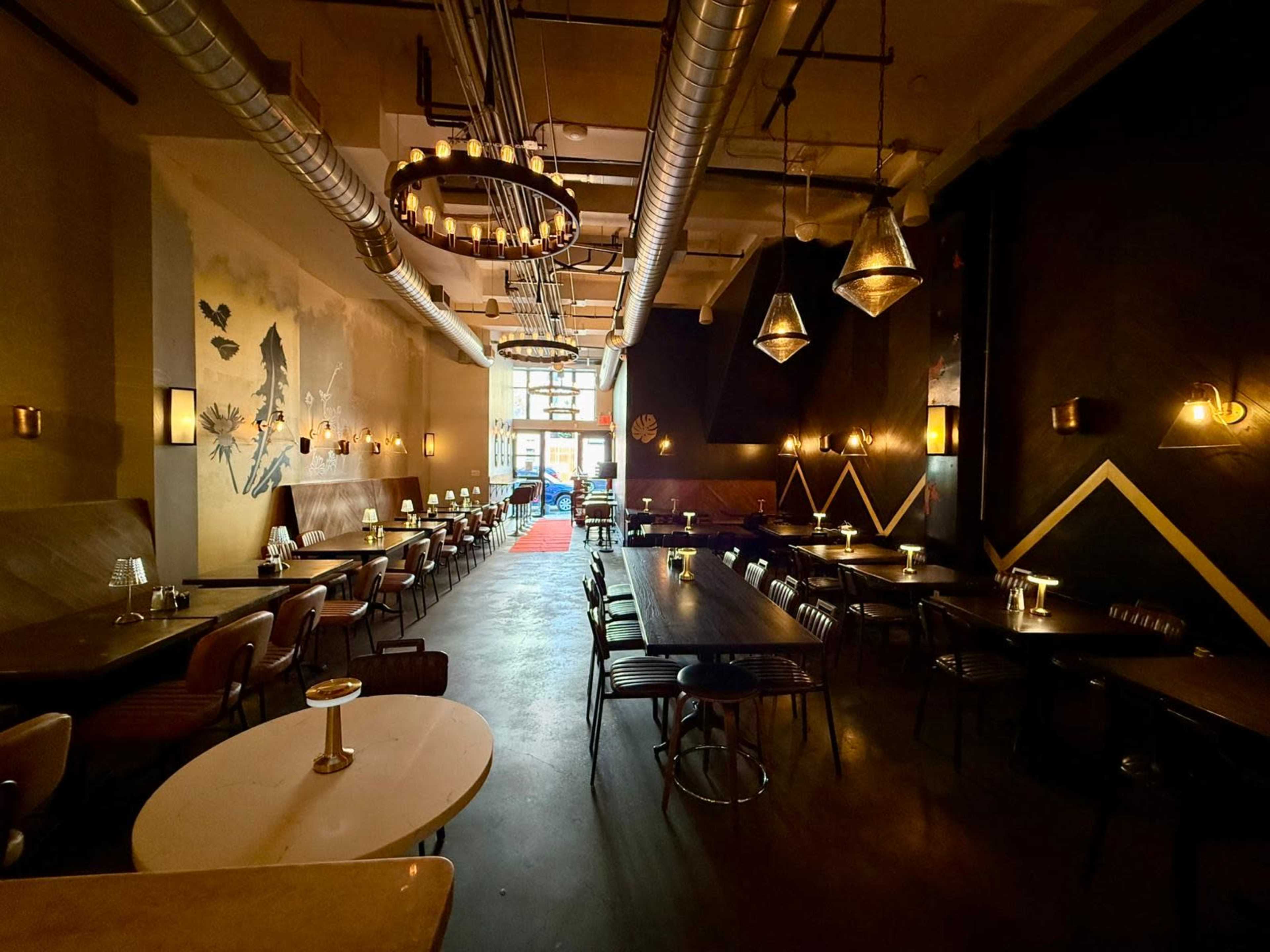 The image shows the interior of a restaurant with rows of tables, pendant lighting, and a decorative mural on the wall.