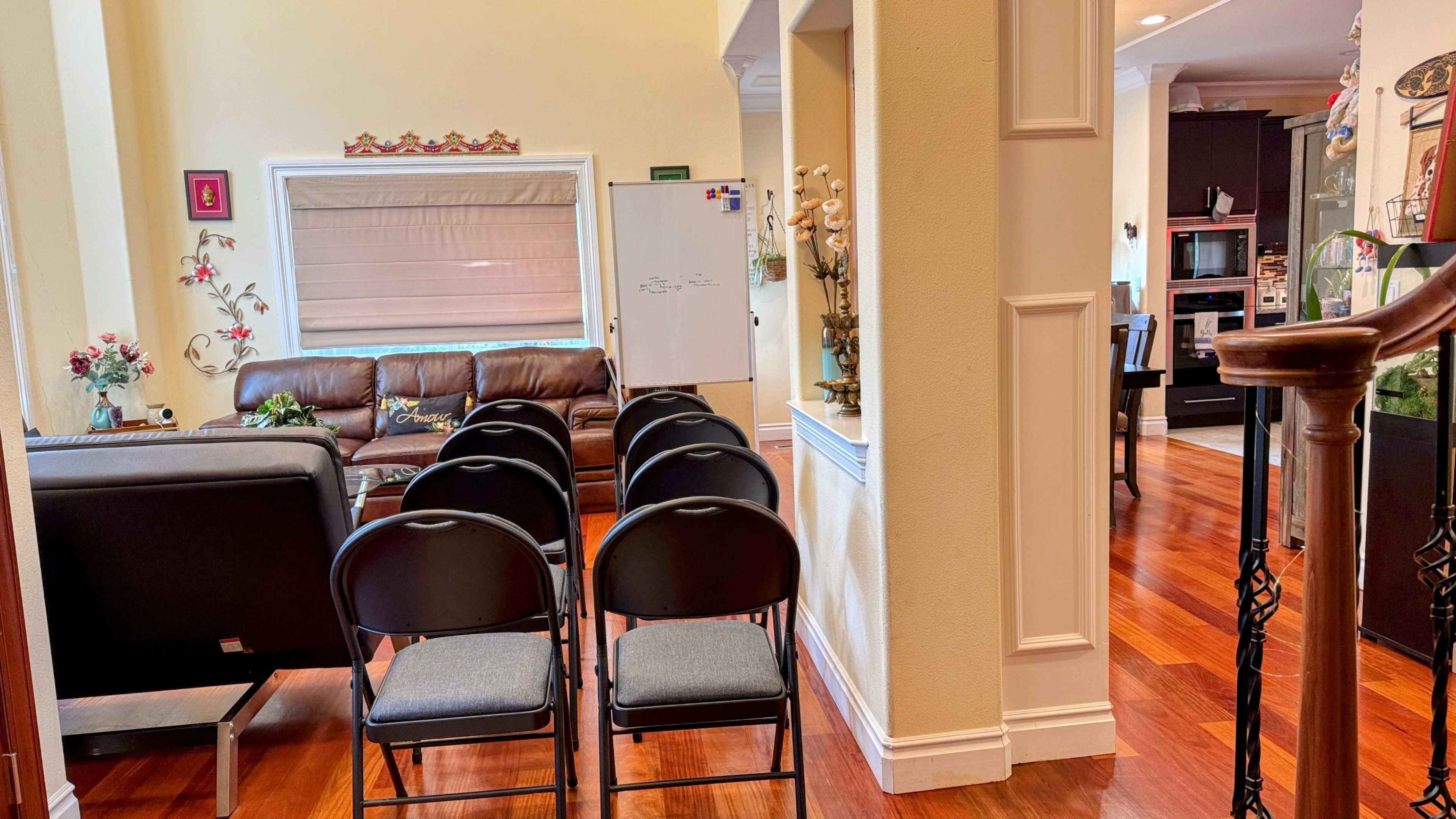 The image shows a living area with a brown leather couch, a row of black folding chairs, and a dining area visible in the background.