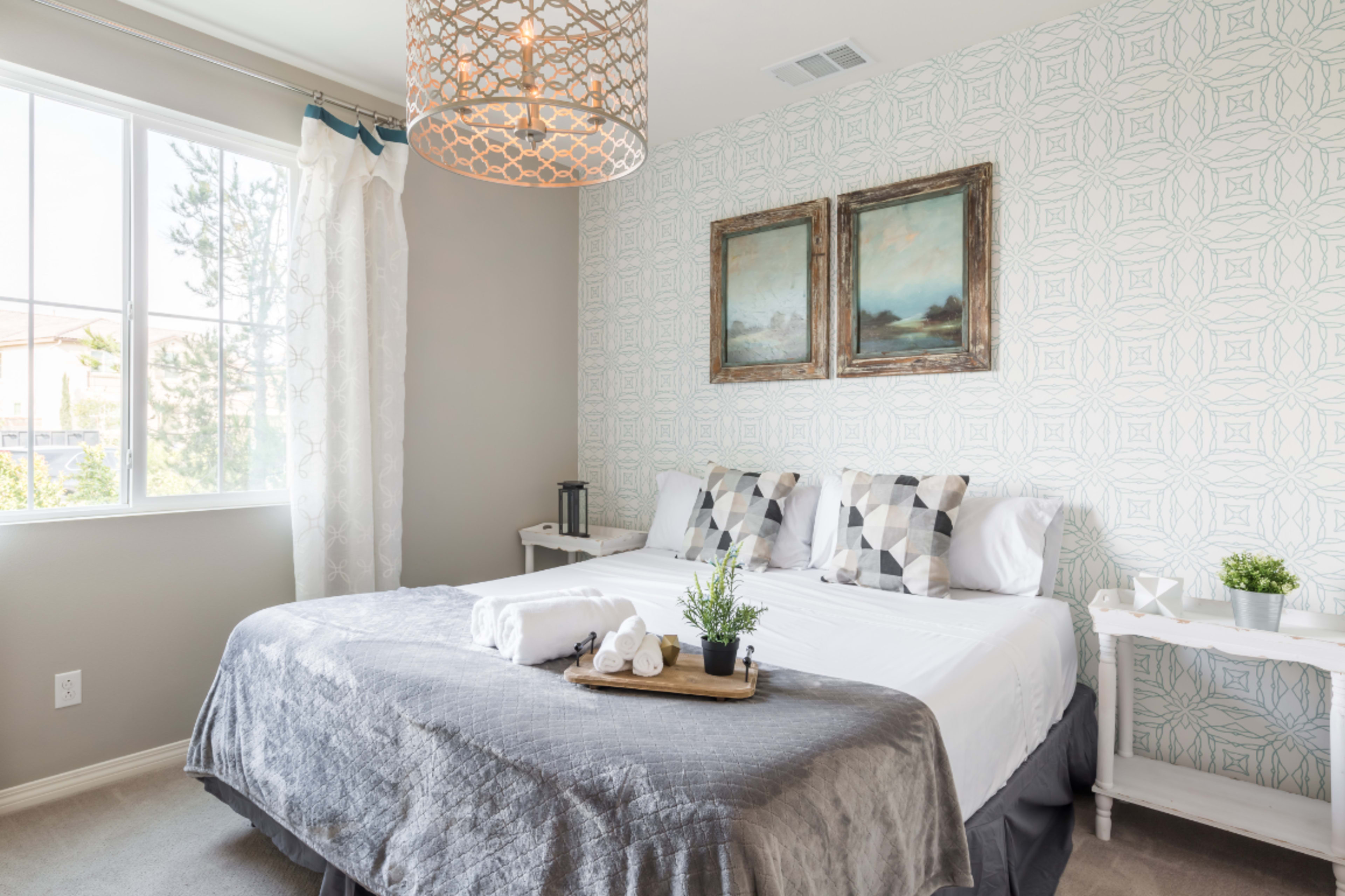 A well-decorated bedroom featuring a large bed with patterned pillows, a tray with towels and a potted plant, and two framed paintings on the wall.