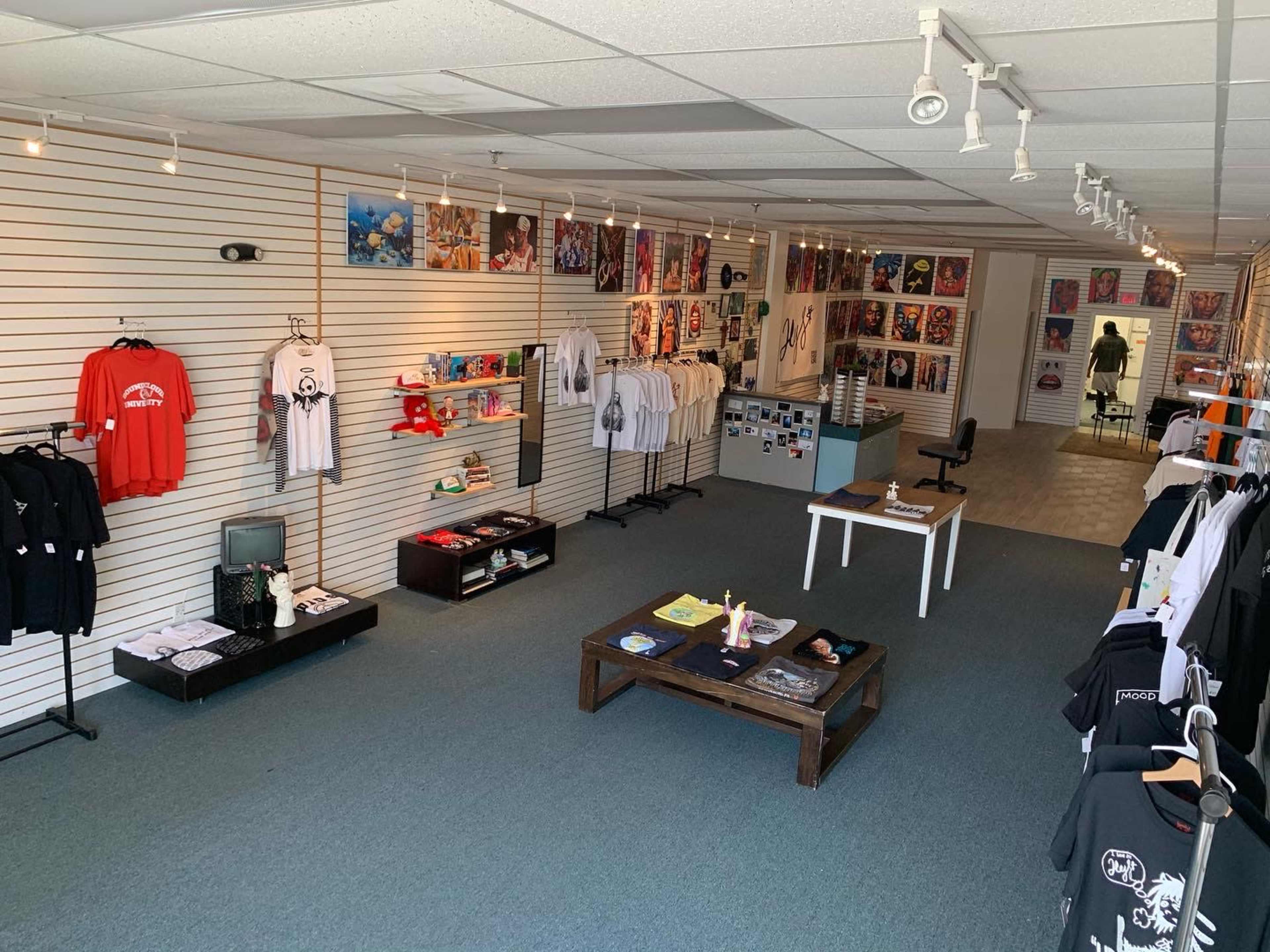 The image shows an art and merchandise store with clothing displayed on racks and various artworks hanging on the walls.