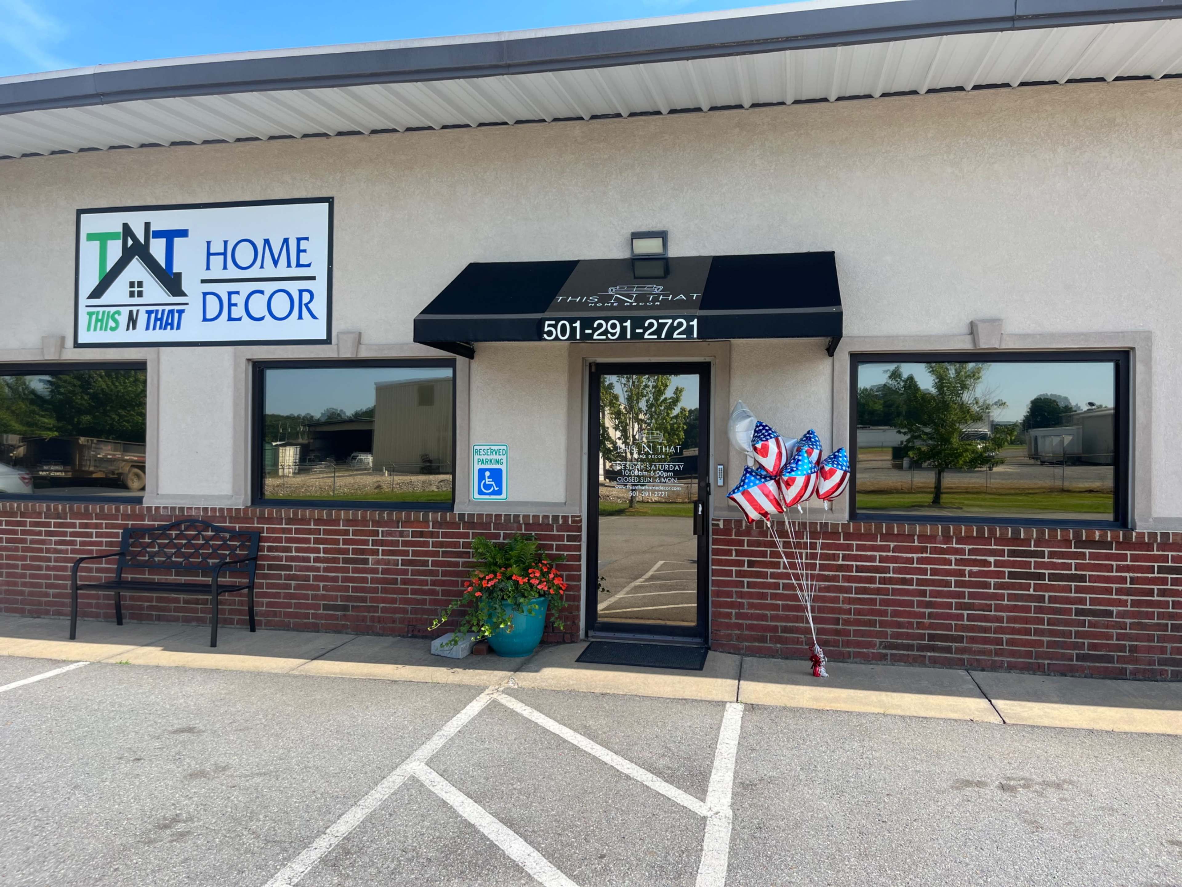 The entrance of a home decor store named "This N That" features a black awning, a potted plant, and balloons with American flags.
