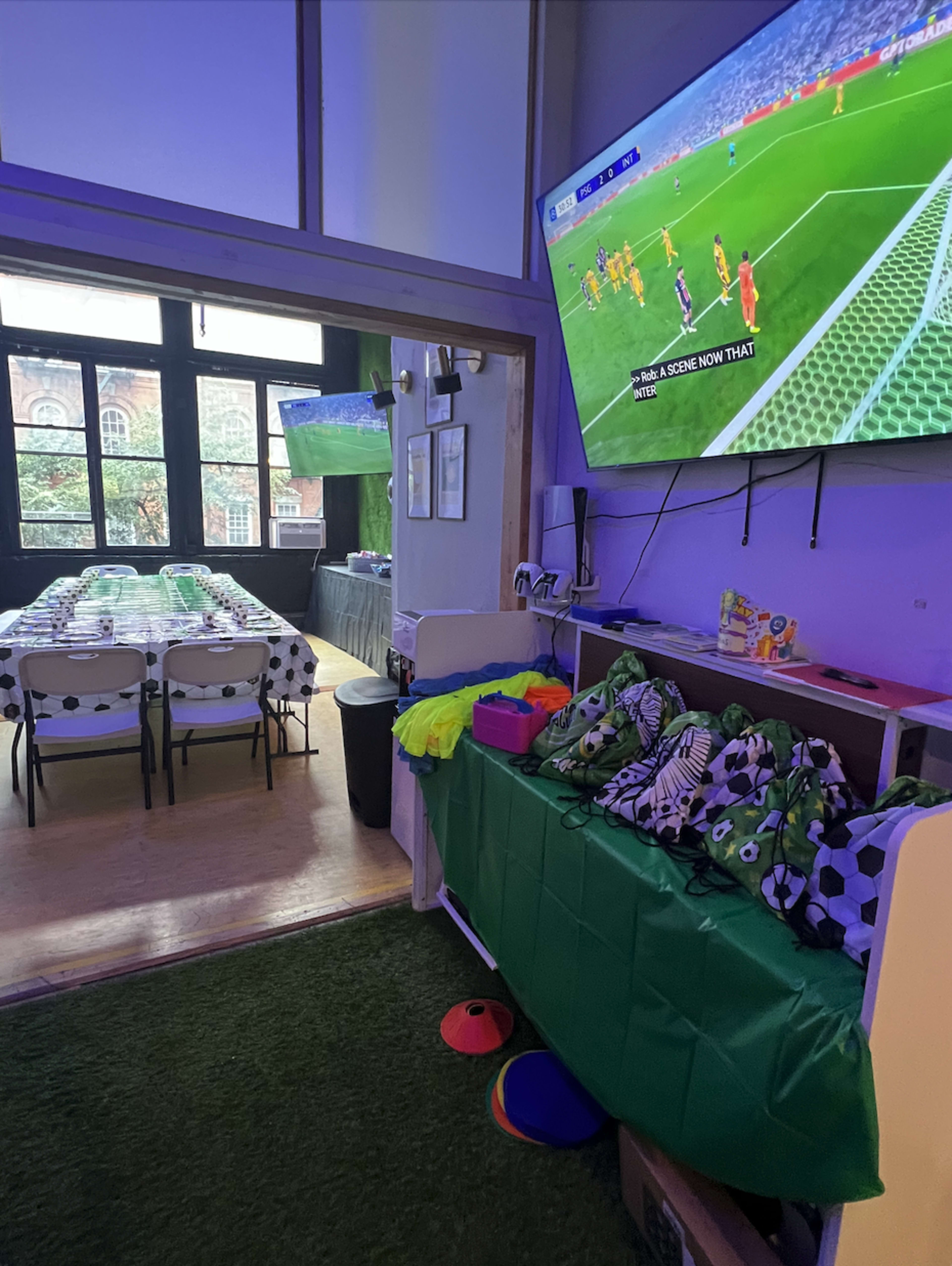 The scene features a decorated event space for a soccer-themed party, with a large screen displaying a game and tables set for guests.