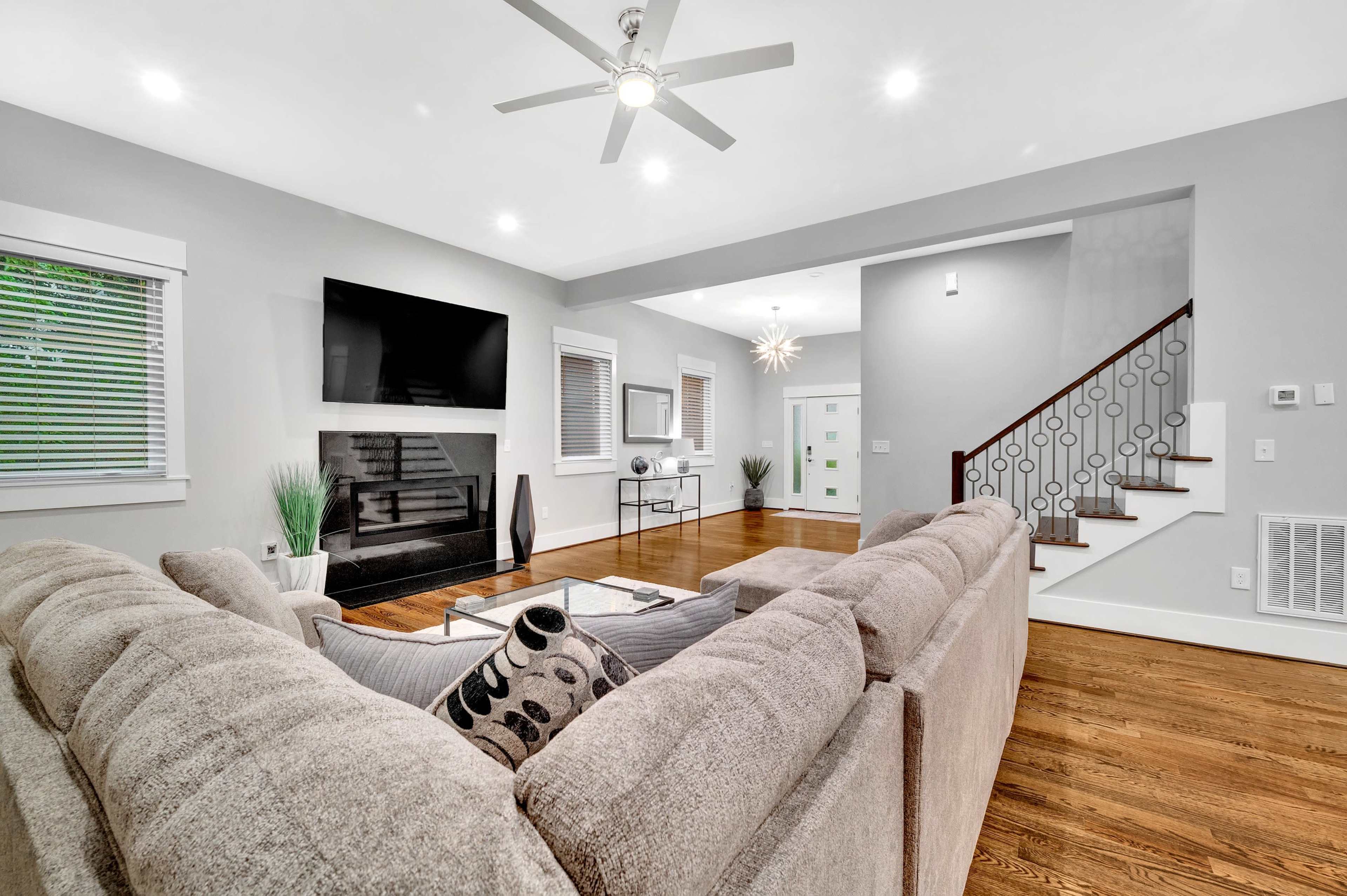 A spacious living room features a sectional sofa, a wall-mounted television, a fireplace, and a staircase leading to an upper level.
