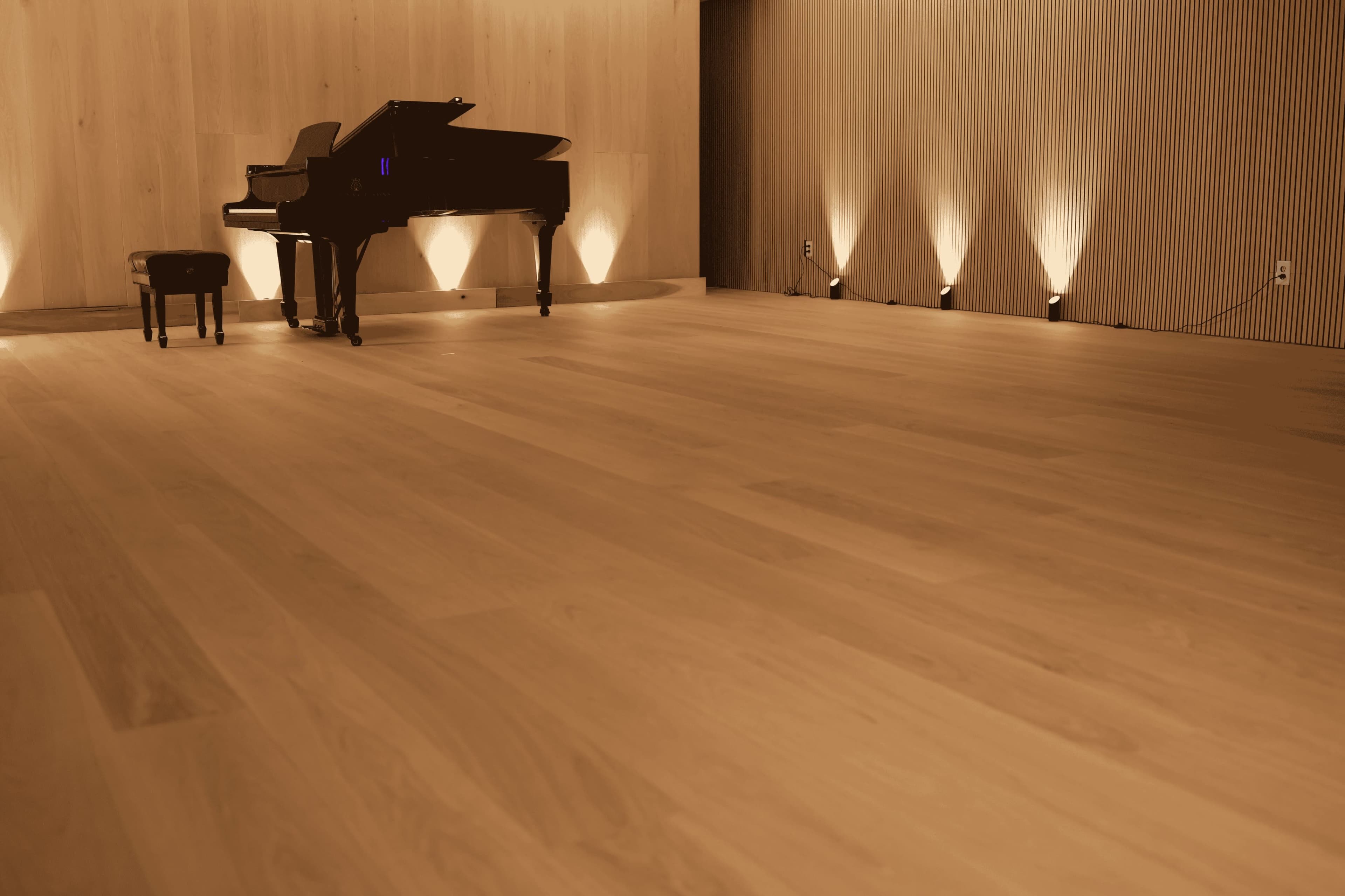 A grand piano and a matching stool are positioned in a softly lit room with wooden walls and a smooth wooden floor.