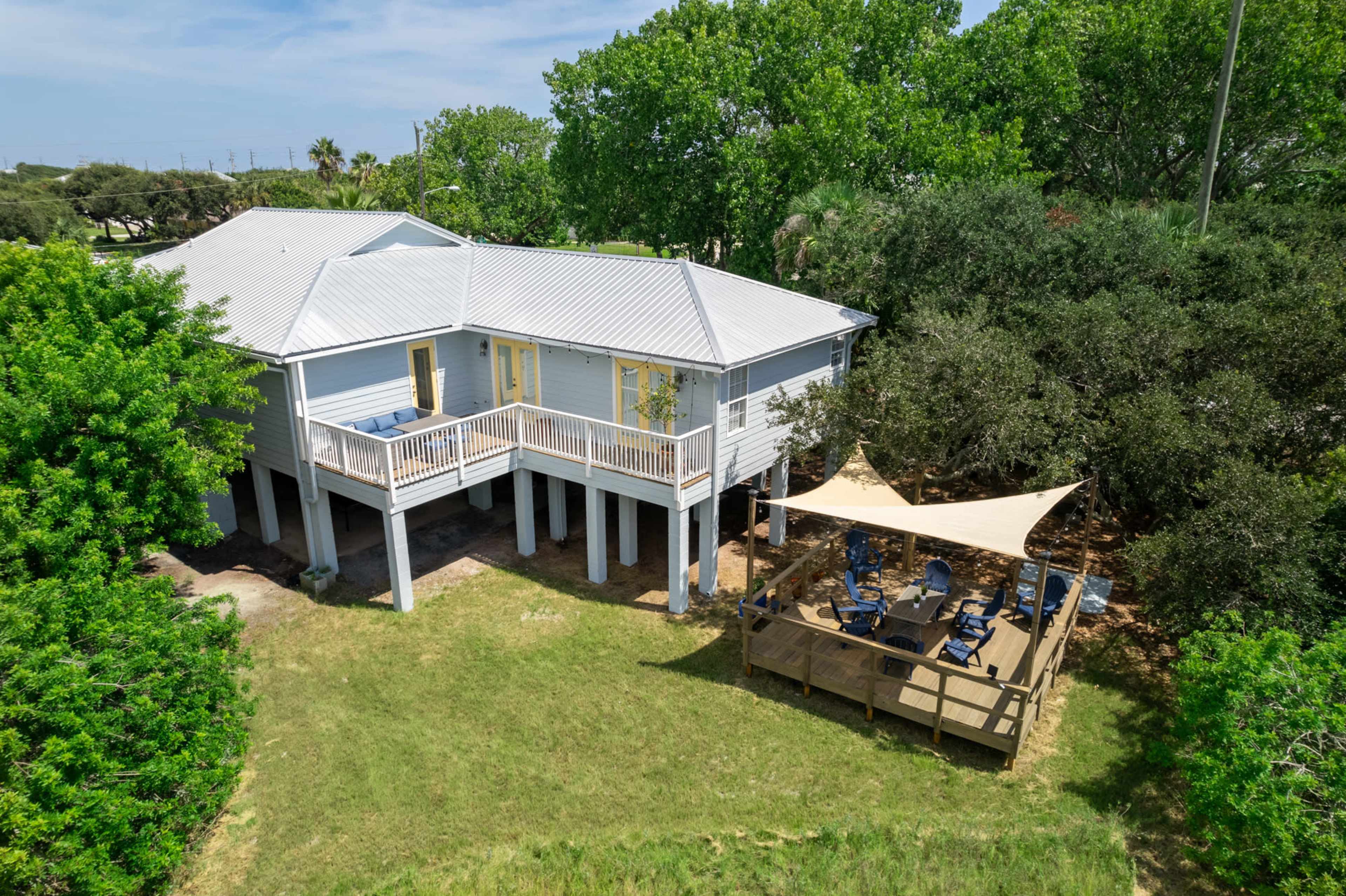 A two-story house with a metal roof stands near a shaded deck area covered by a canopy.
