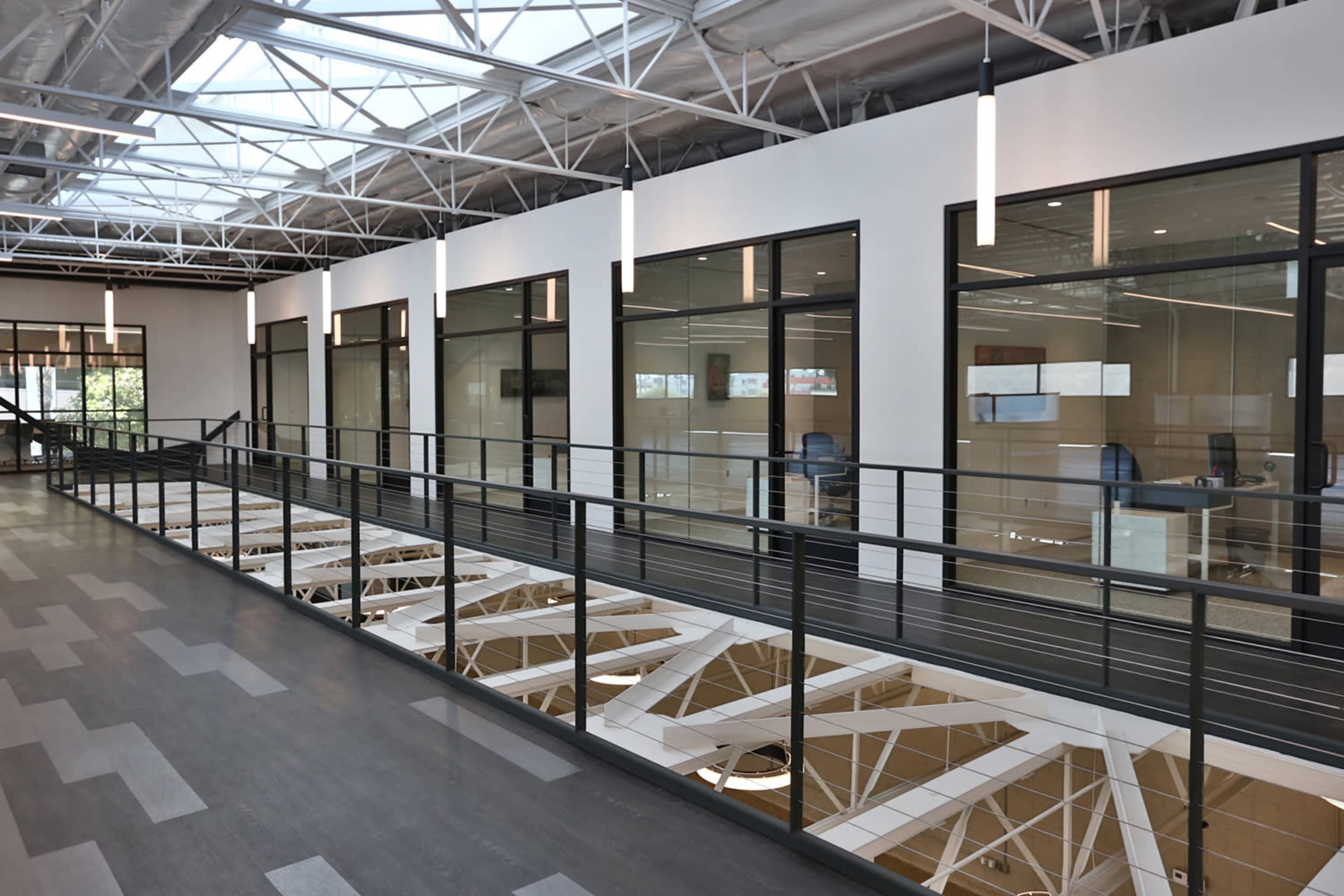 A modern office space with a second-floor balcony overlooking open workstations and large windows.
