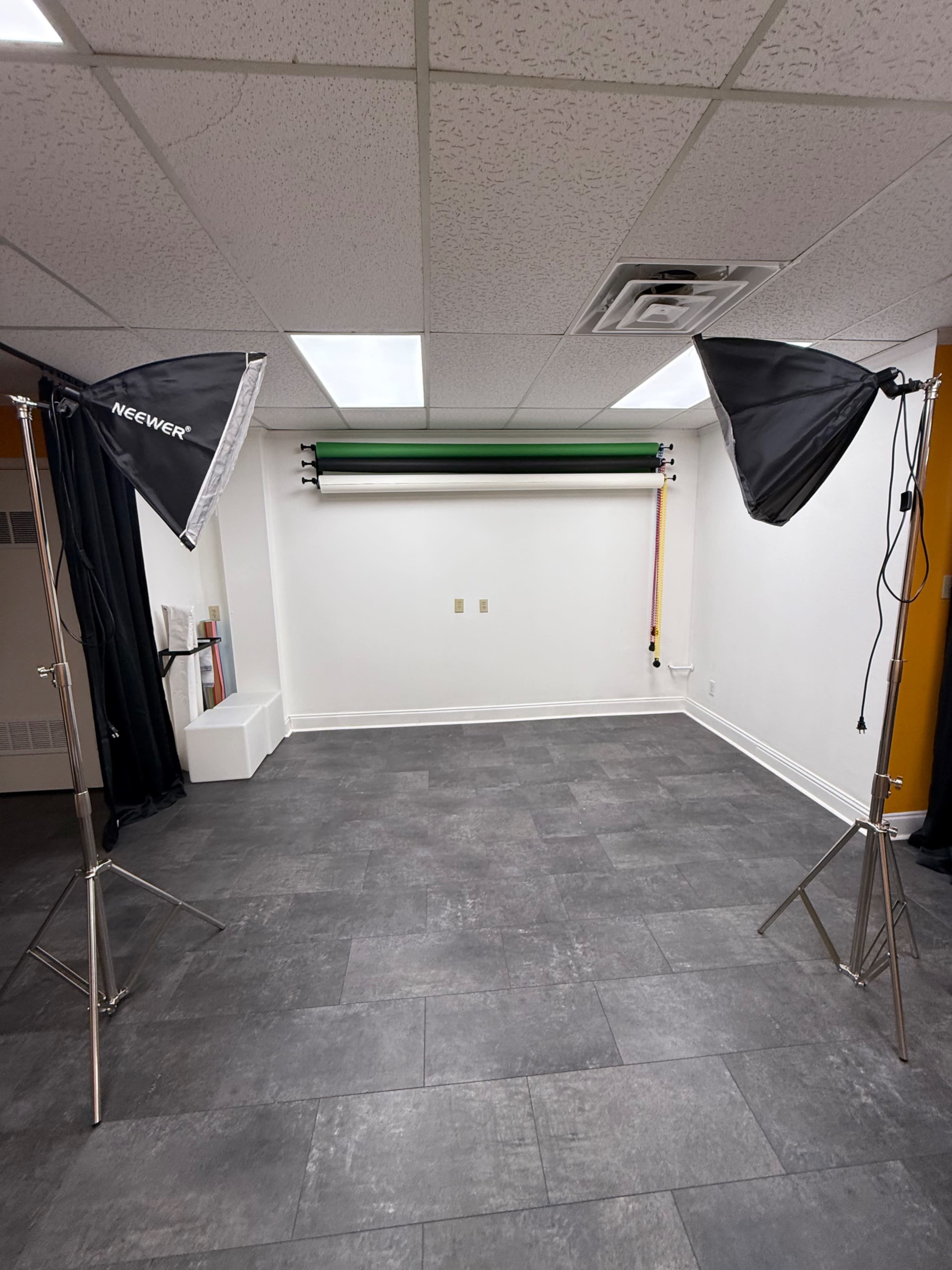 The image shows an empty studio space with two lighting umbrellas on tripods and a green backdrop set up on the wall.