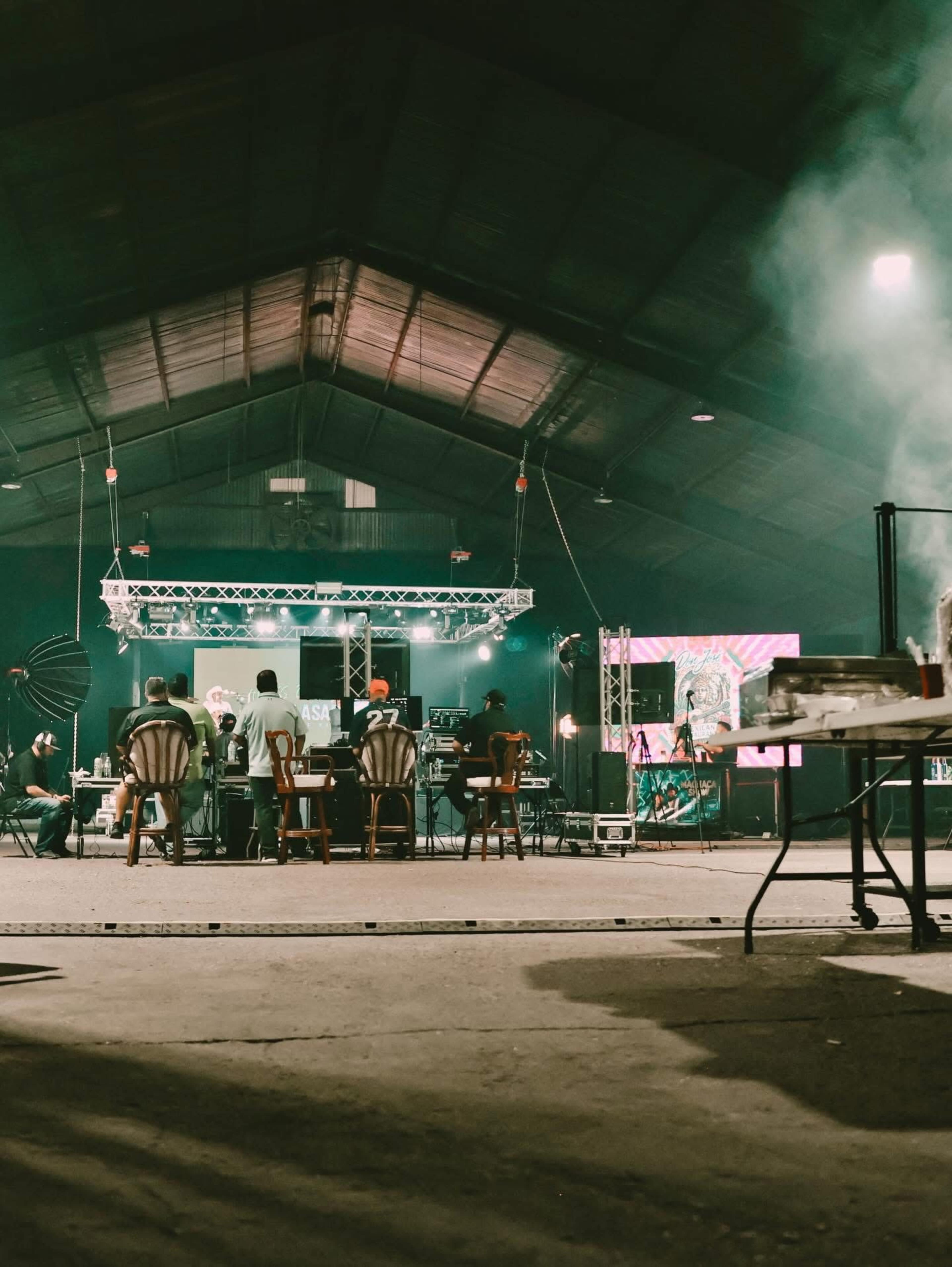 A group of people works on a stage setup inside a large, dimly lit warehouse.