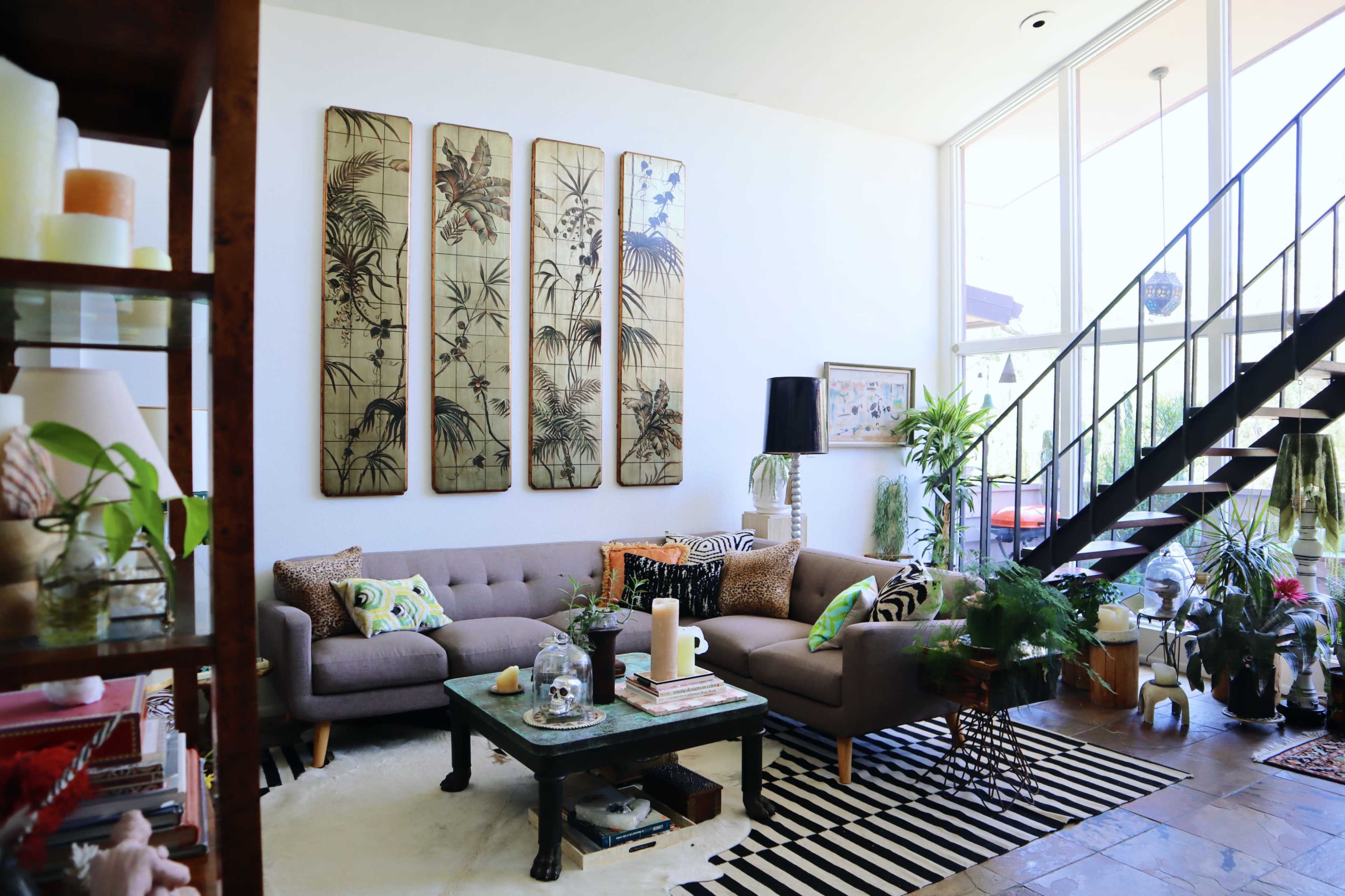 A modern living room features a sectional sofa, decorative plants, and wall art with a staircase in the background.