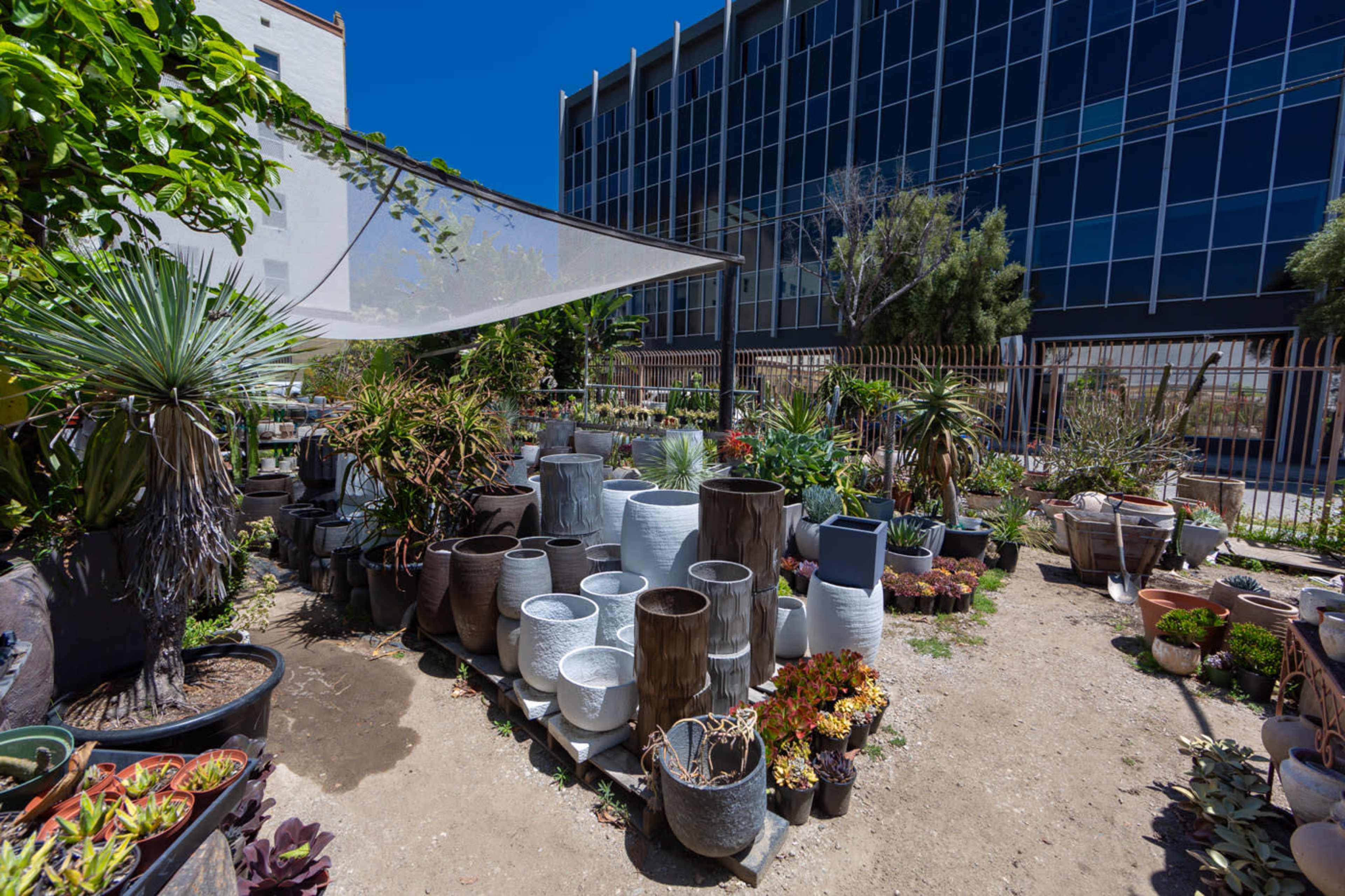 A garden center displays a variety of planters and pots surrounded by various plants against a backdrop of a modern building.