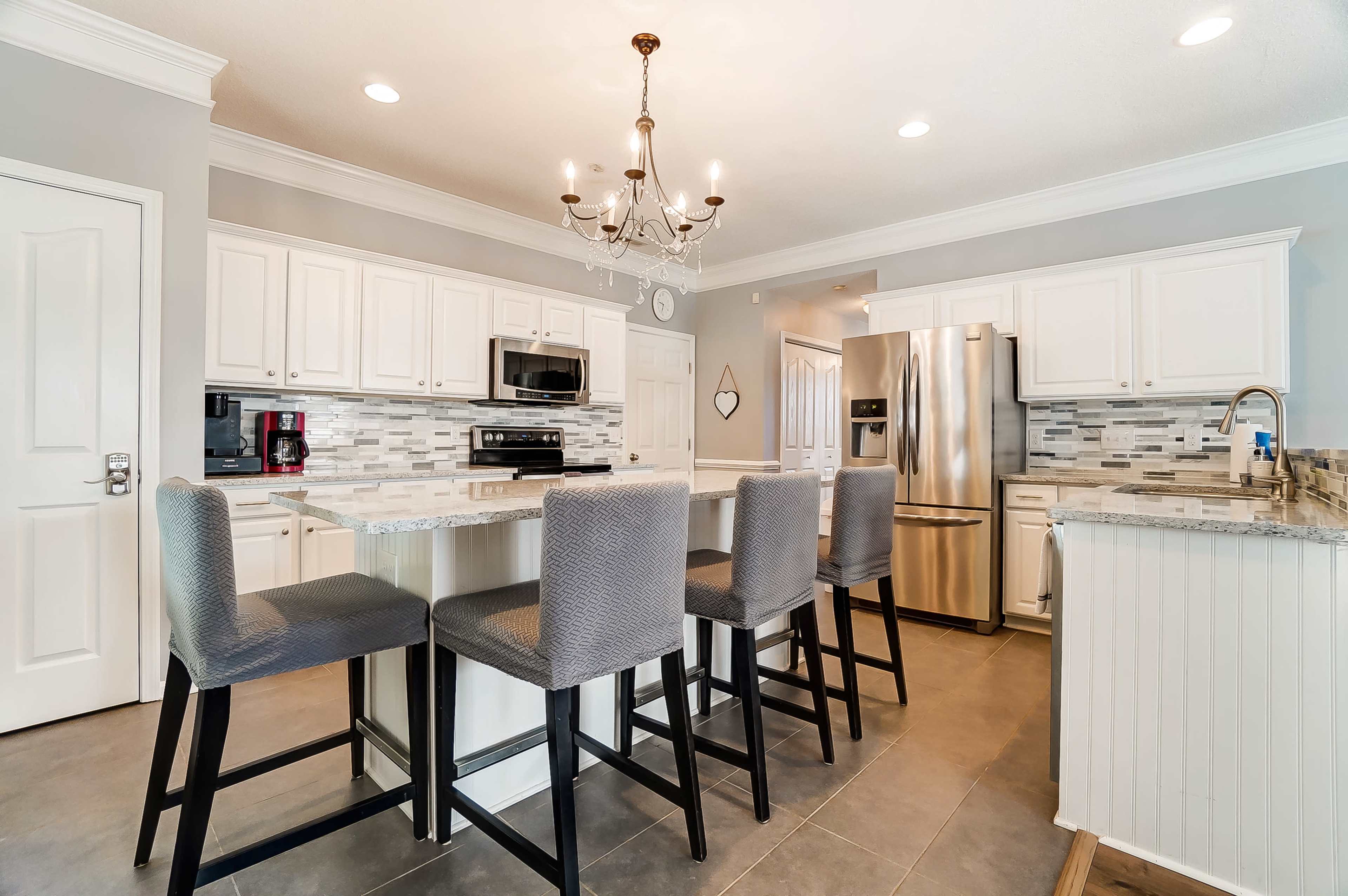 A modern kitchen features white cabinets, a gray countertop, stainless steel appliances, and a large island with seating for four.