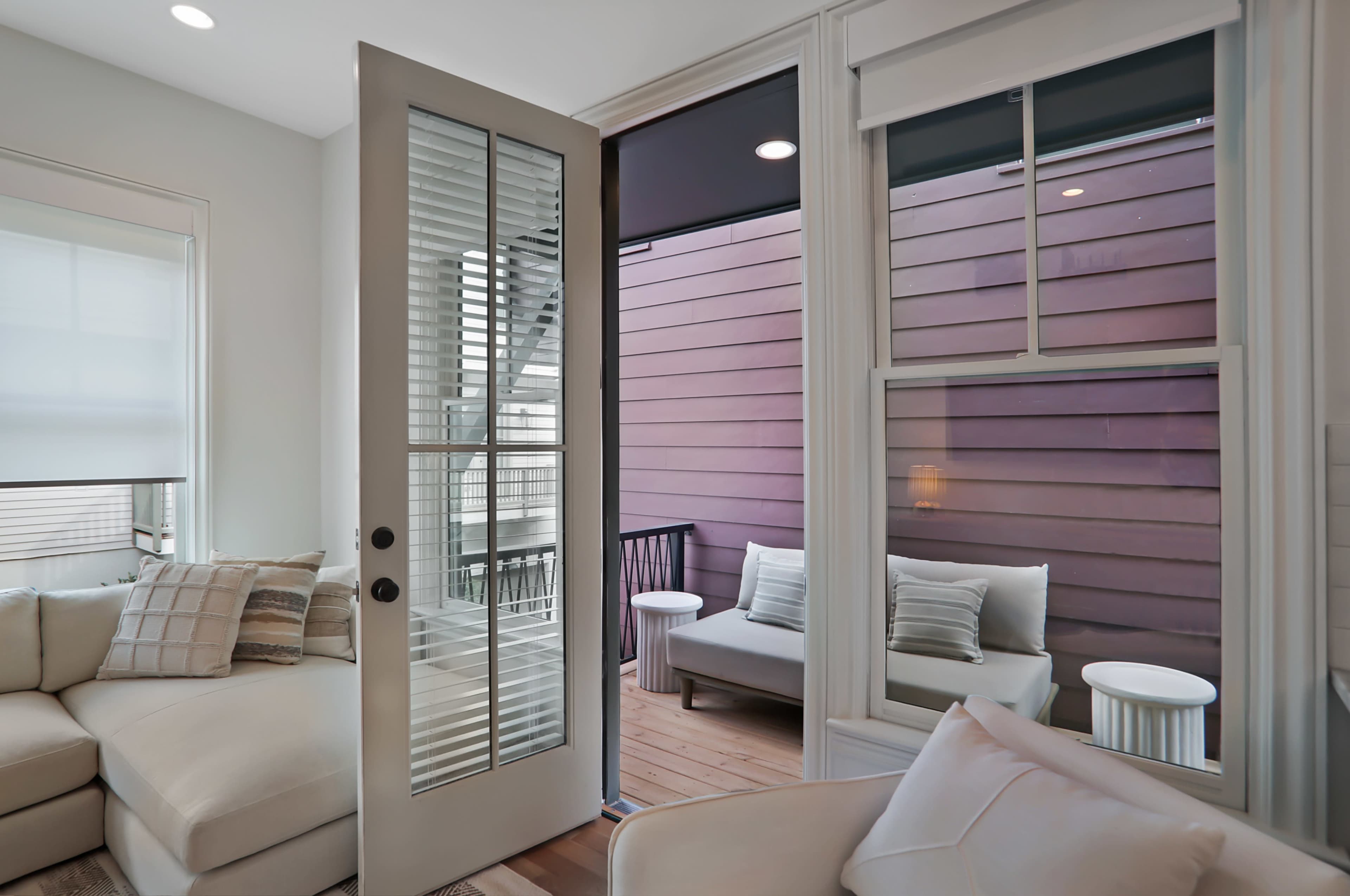 A light-filled living room with a door leading to a small balcony featuring outdoor seating.