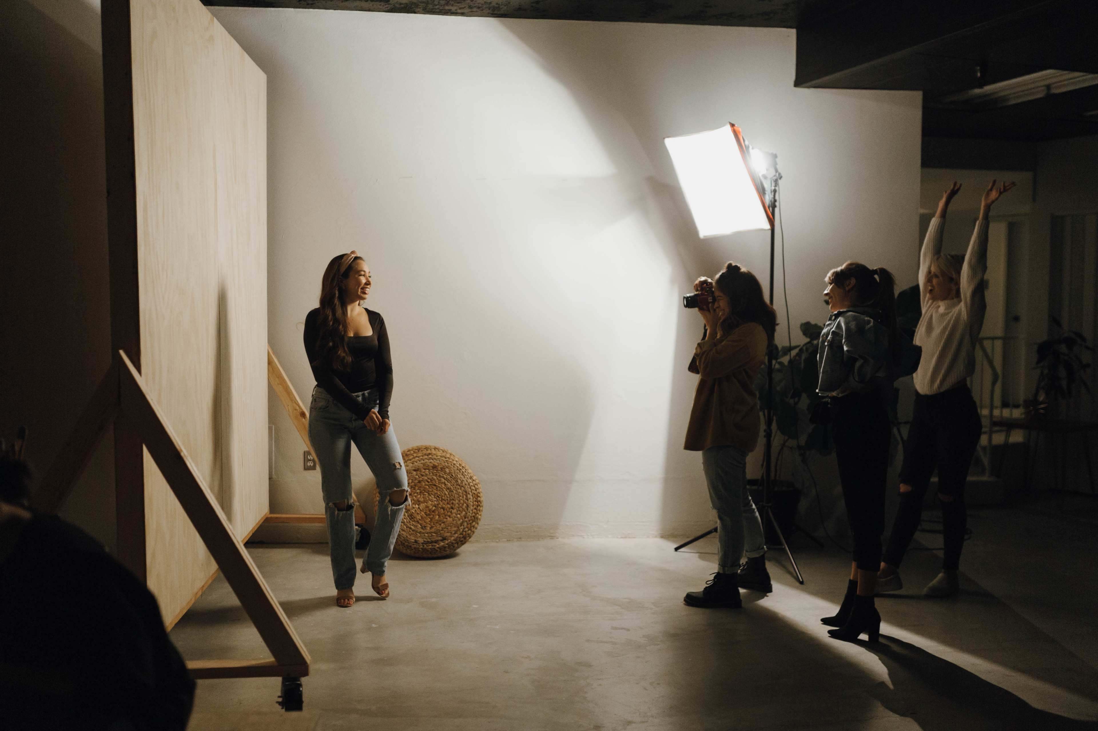 A photographer captures an individual posing in front of a backdrop, while three others celebrate and interact in a well-lit studio space.