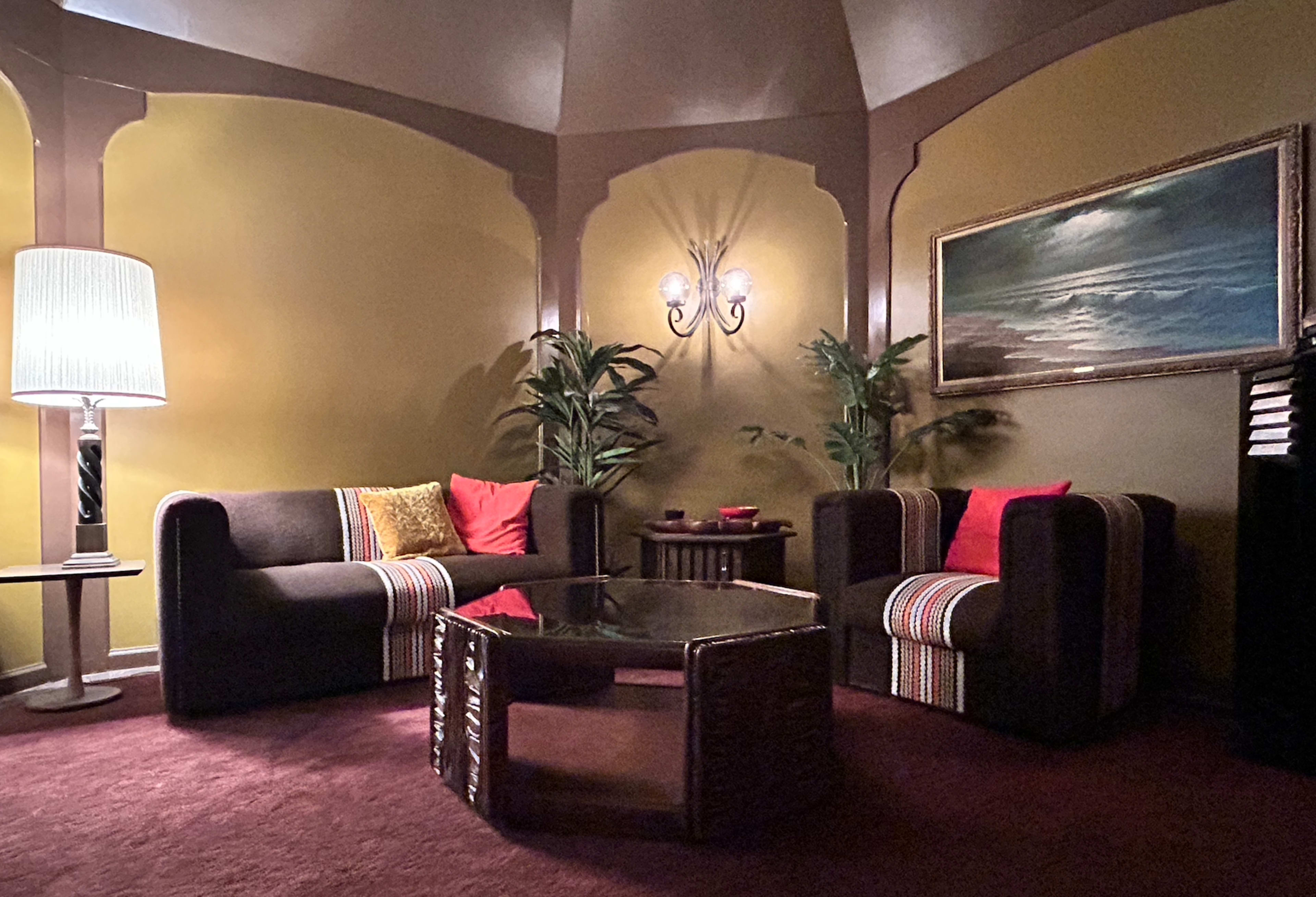 A cozy seating area features two sofas and an armchair around a glass coffee table, with warm wall colors and decorative plants.