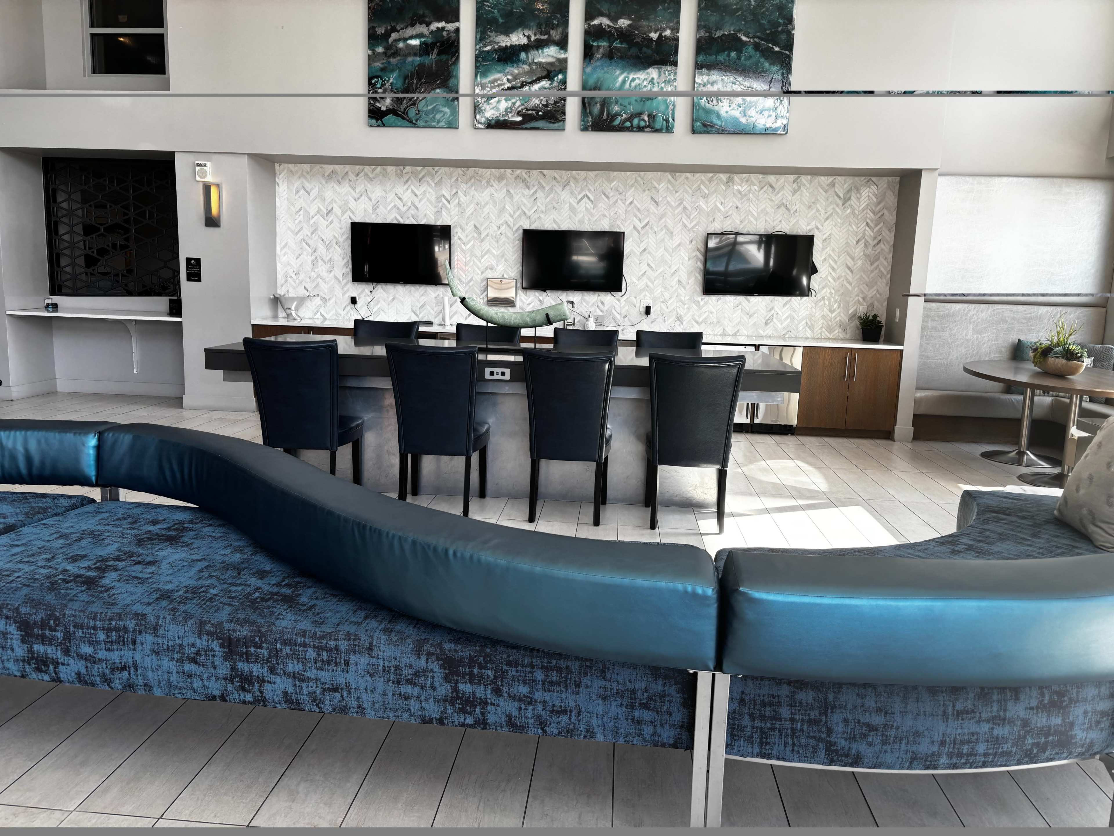 The image features a modern interior space with a curved blue sofa facing a dining area equipped with multiple televisions.