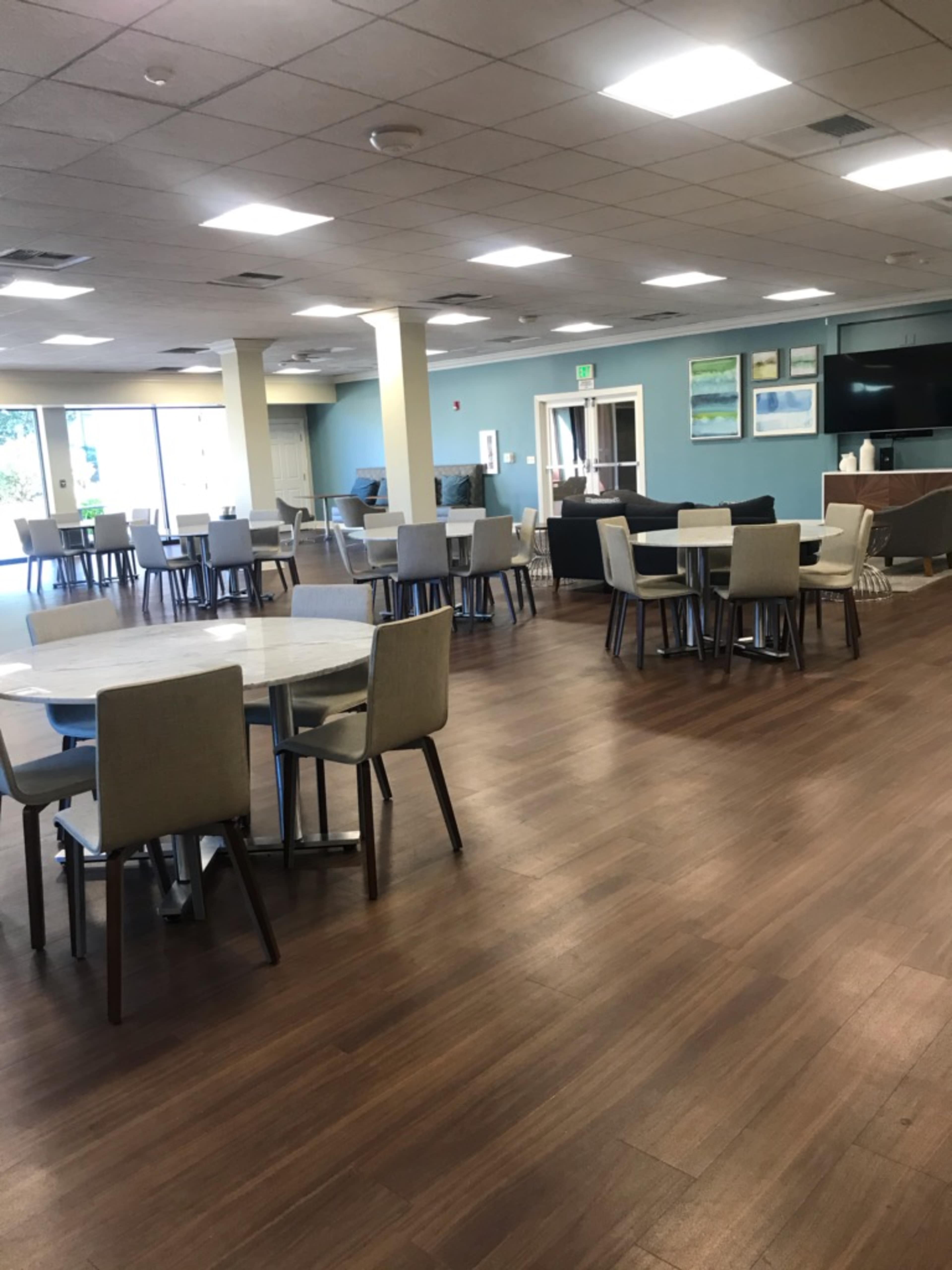 A spacious dining area features several round tables and chairs arranged neatly on a wooden floor.