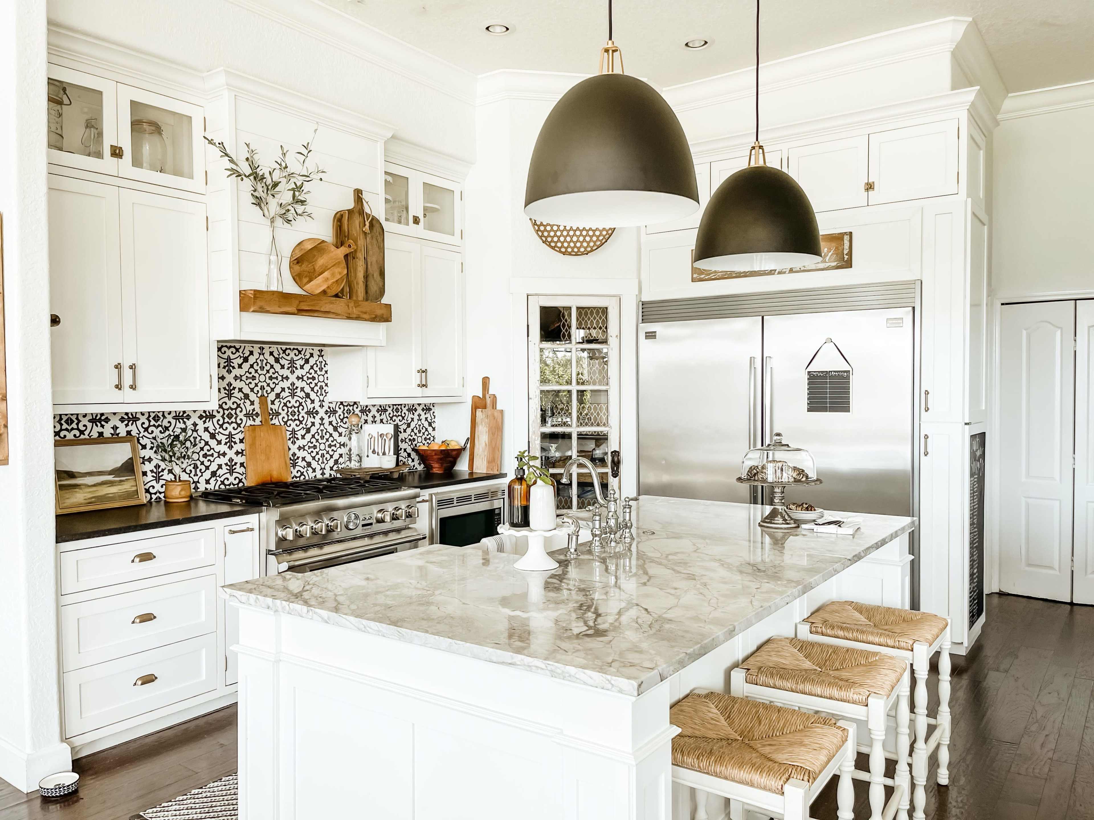The kitchen features white cabinetry, a large marble island with seating, and a combination of modern appliances and decorative wooden accents.