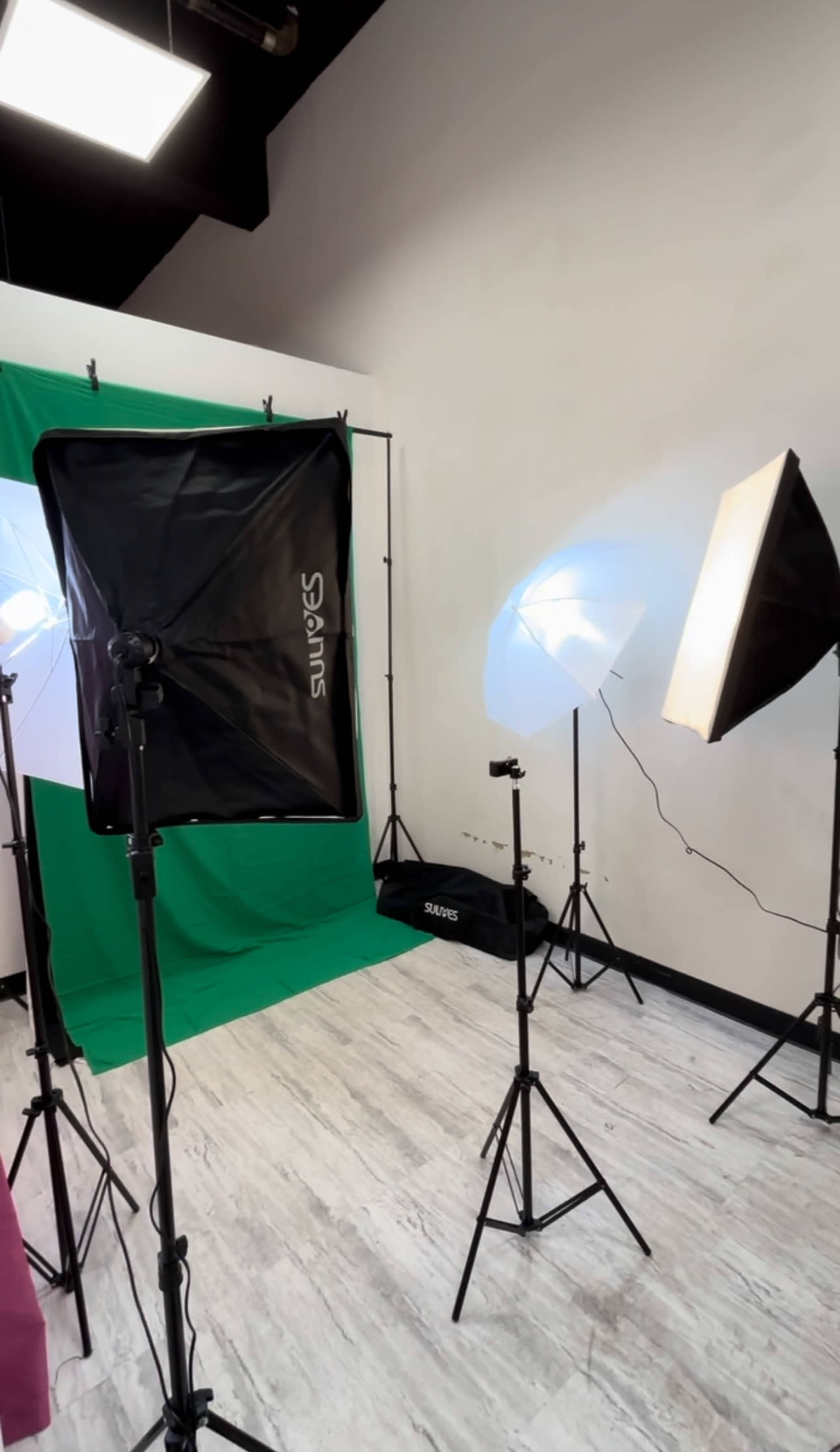 The image shows a photography studio setup with a green backdrop and various lighting equipment positioned around the area.