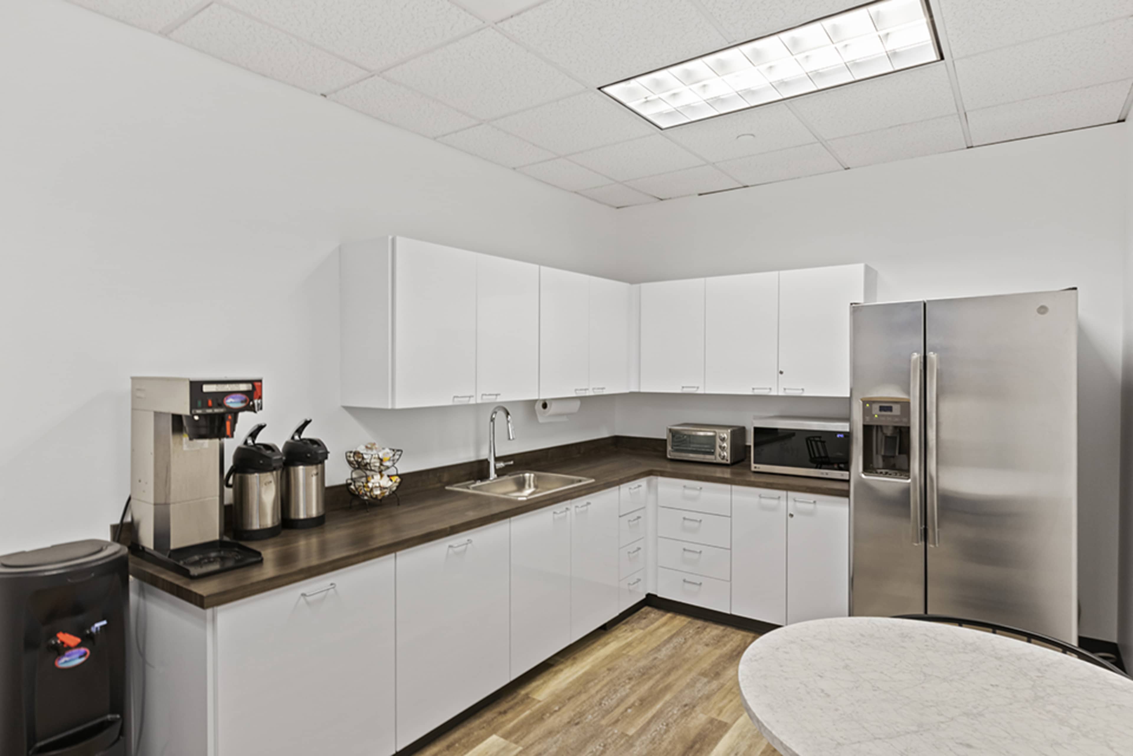 A modern kitchen equipped with white cabinets, a stainless steel refrigerator, and appliances including a coffee maker and microwave.
