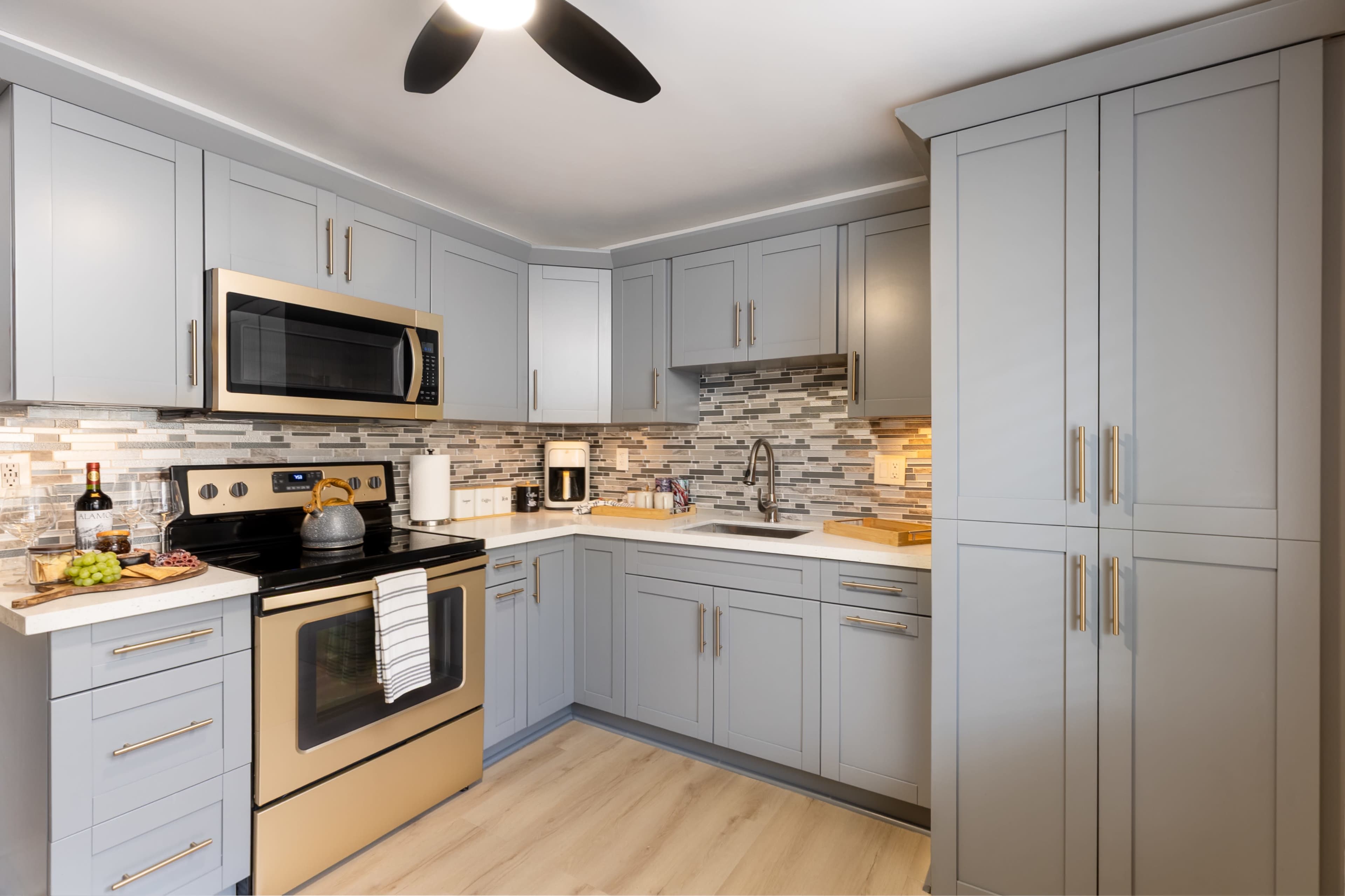The kitchen features gray cabinetry, a stainless steel microwave and oven, and a mosaic tile backsplash.