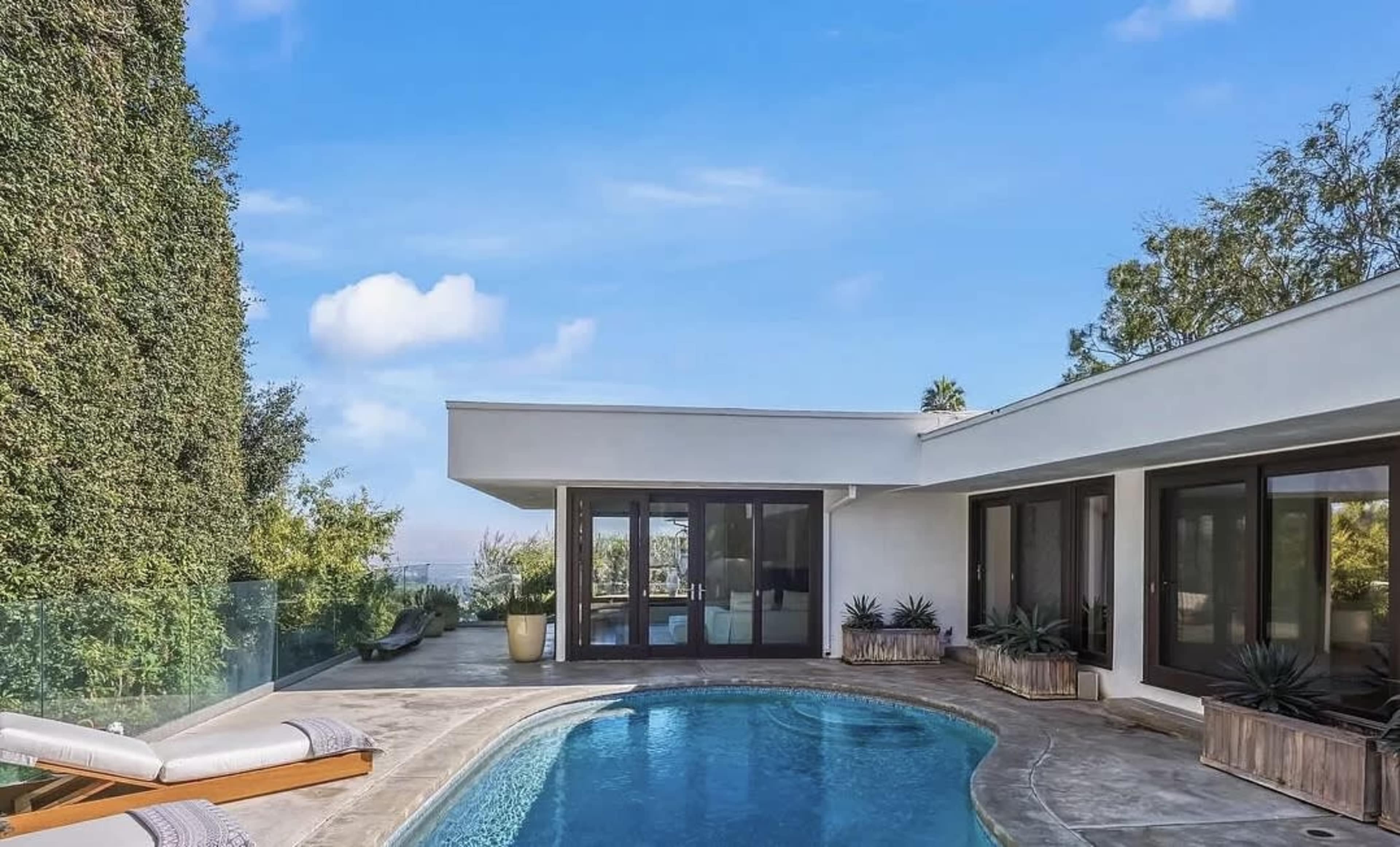 A modern home with a swimming pool, surrounded by greenery and a clear blue sky.