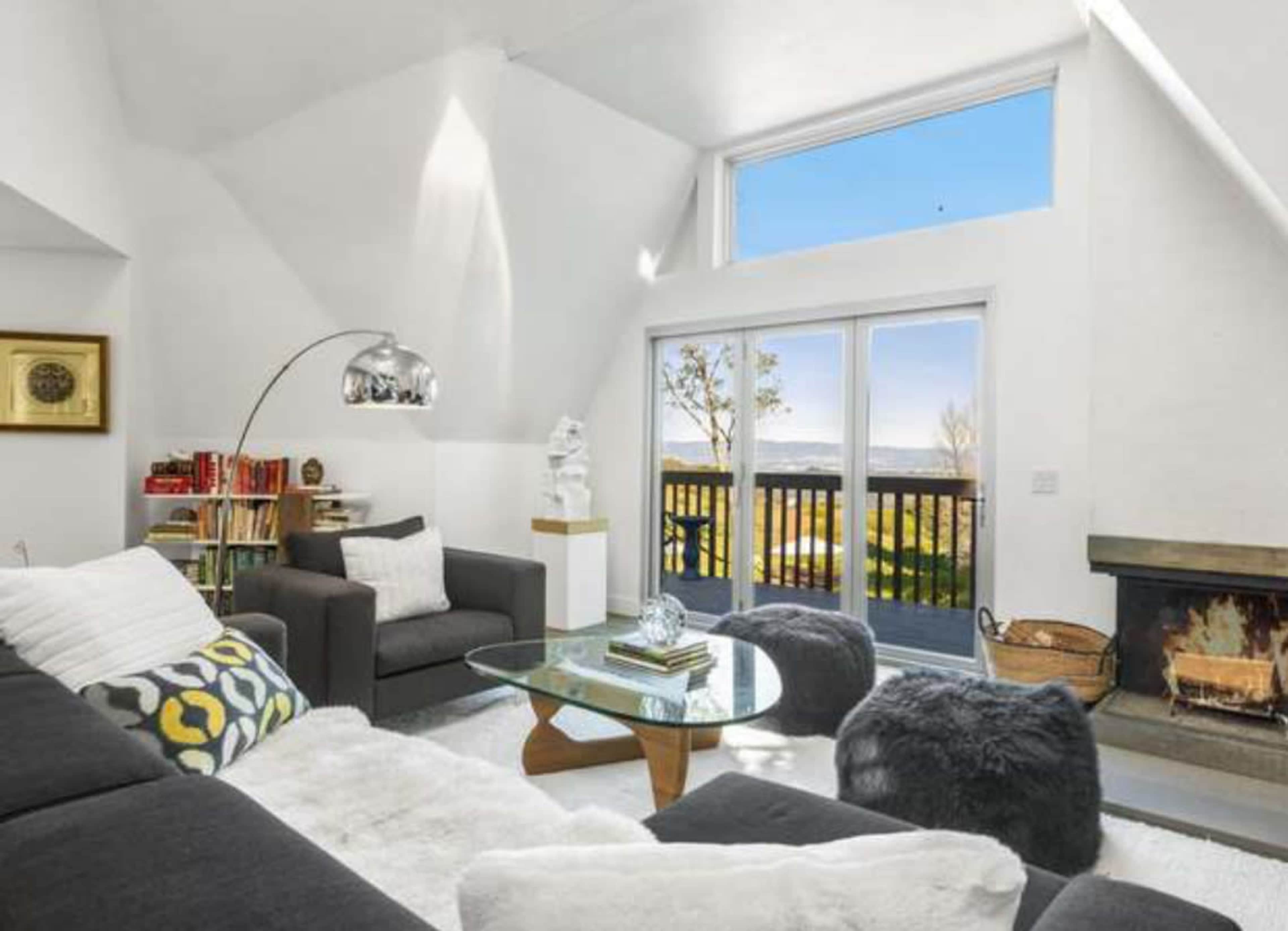 A modern living room features a dark sectional sofa, a glass coffee table, and large windows that overlook a scenic view.