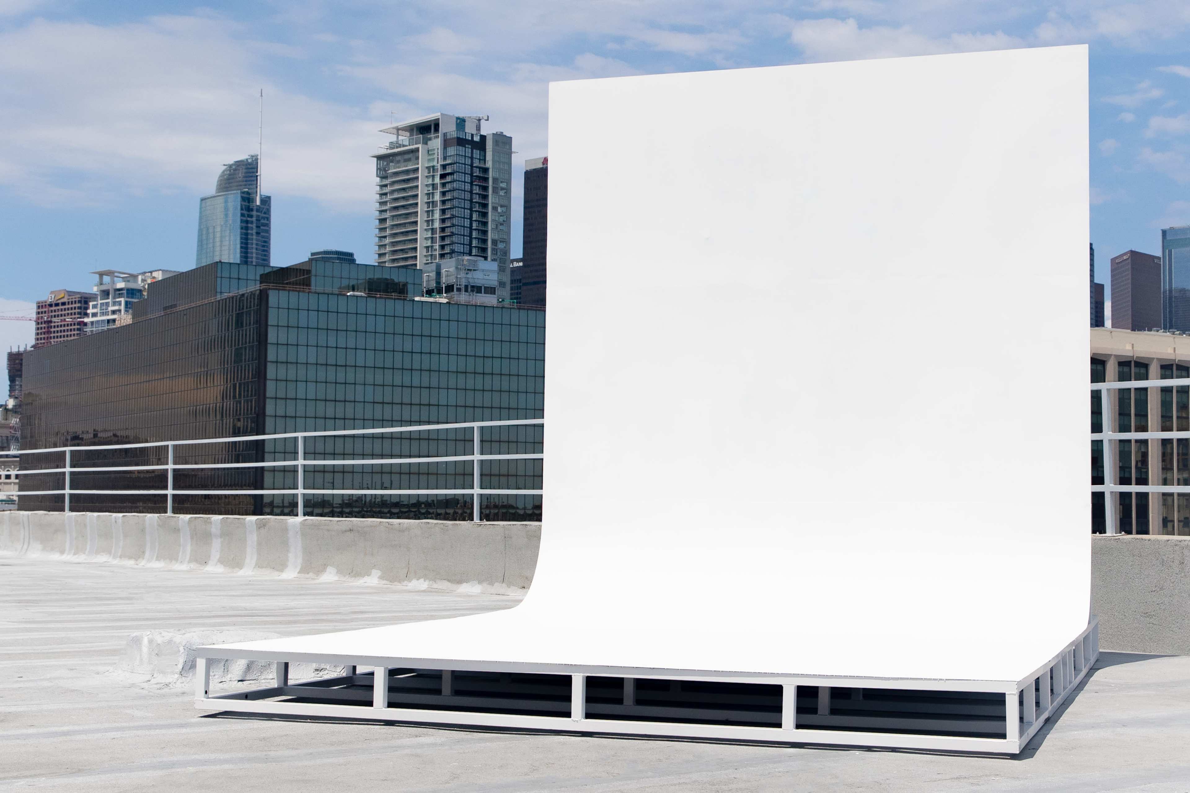 A white backdrop is positioned on a rooftop with a city skyline in the background.