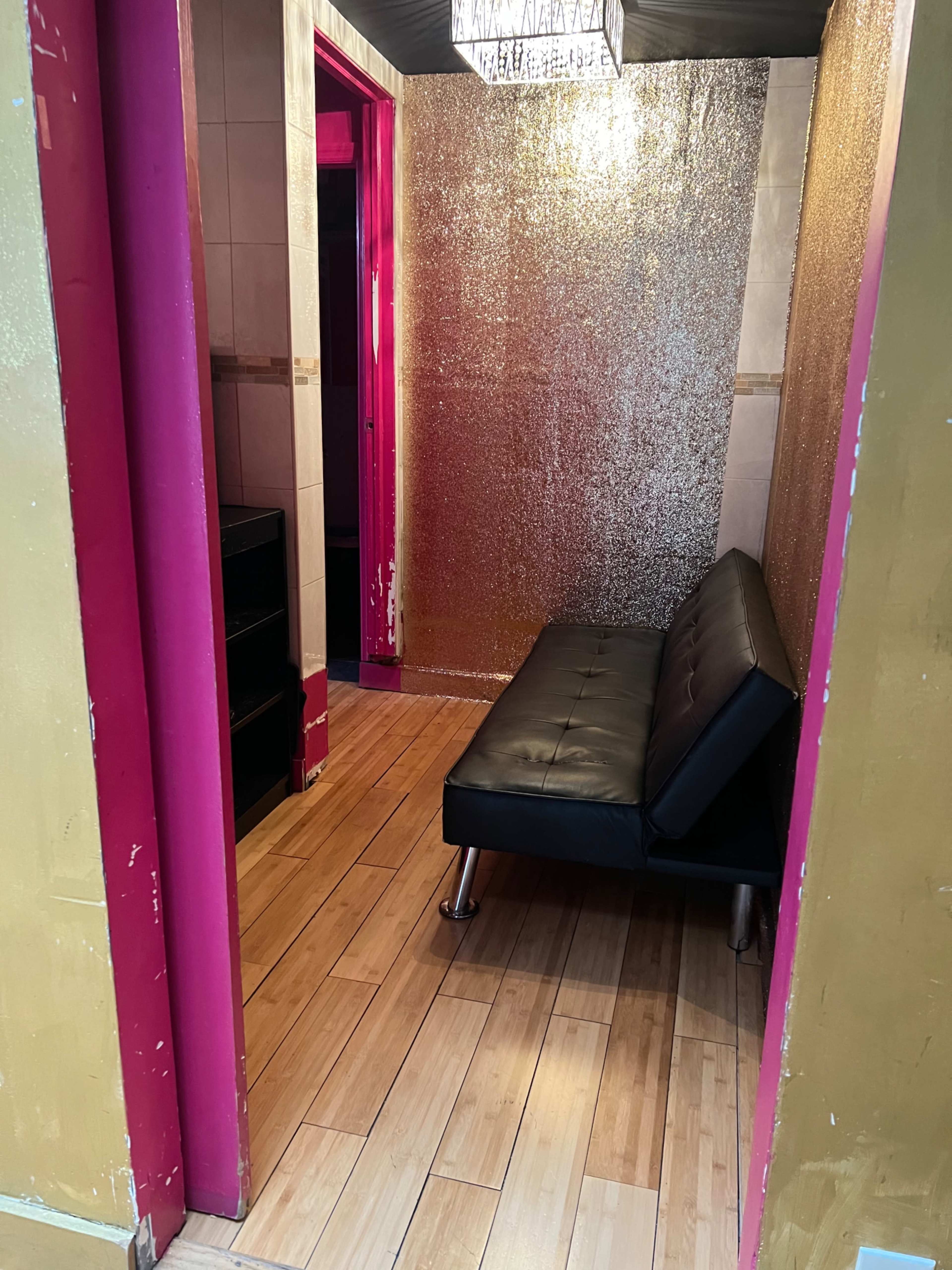 A small room featuring a black futon, a shiny metallic wall, and wooden flooring.