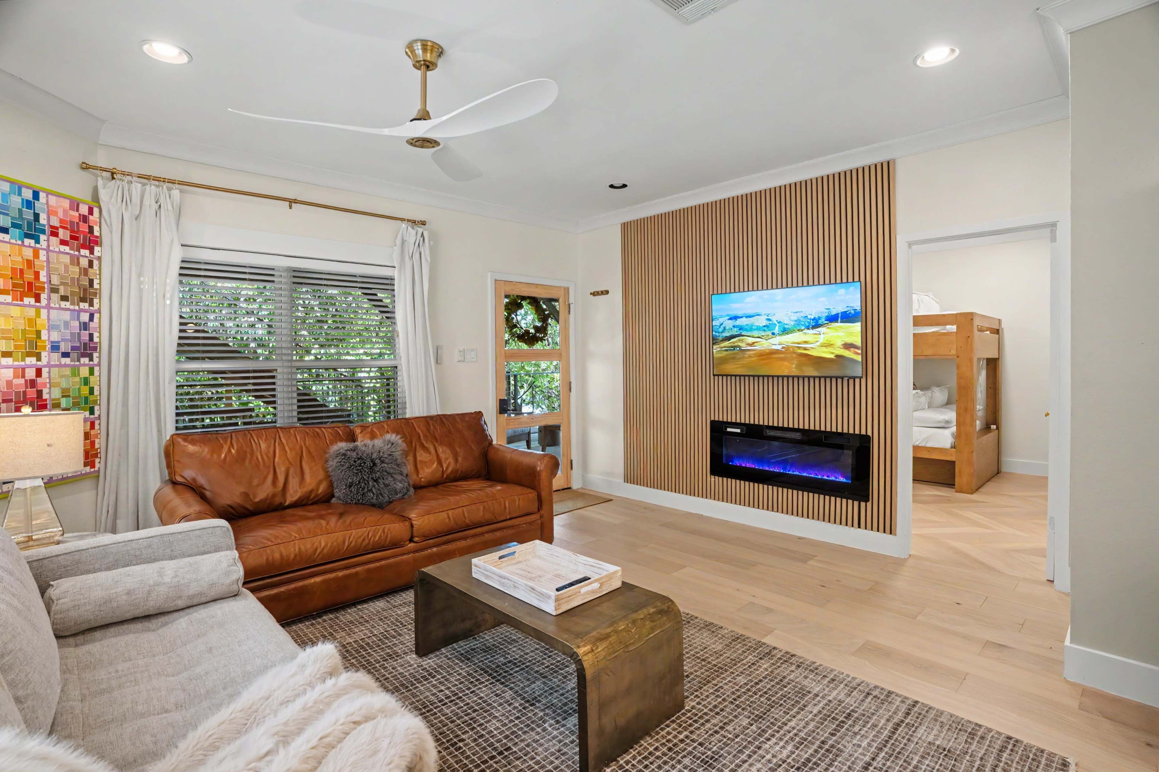The scene shows a modern living room with a brown leather sofa, a coffee table, a wall-mounted TV, and a decorative wood panel feature.