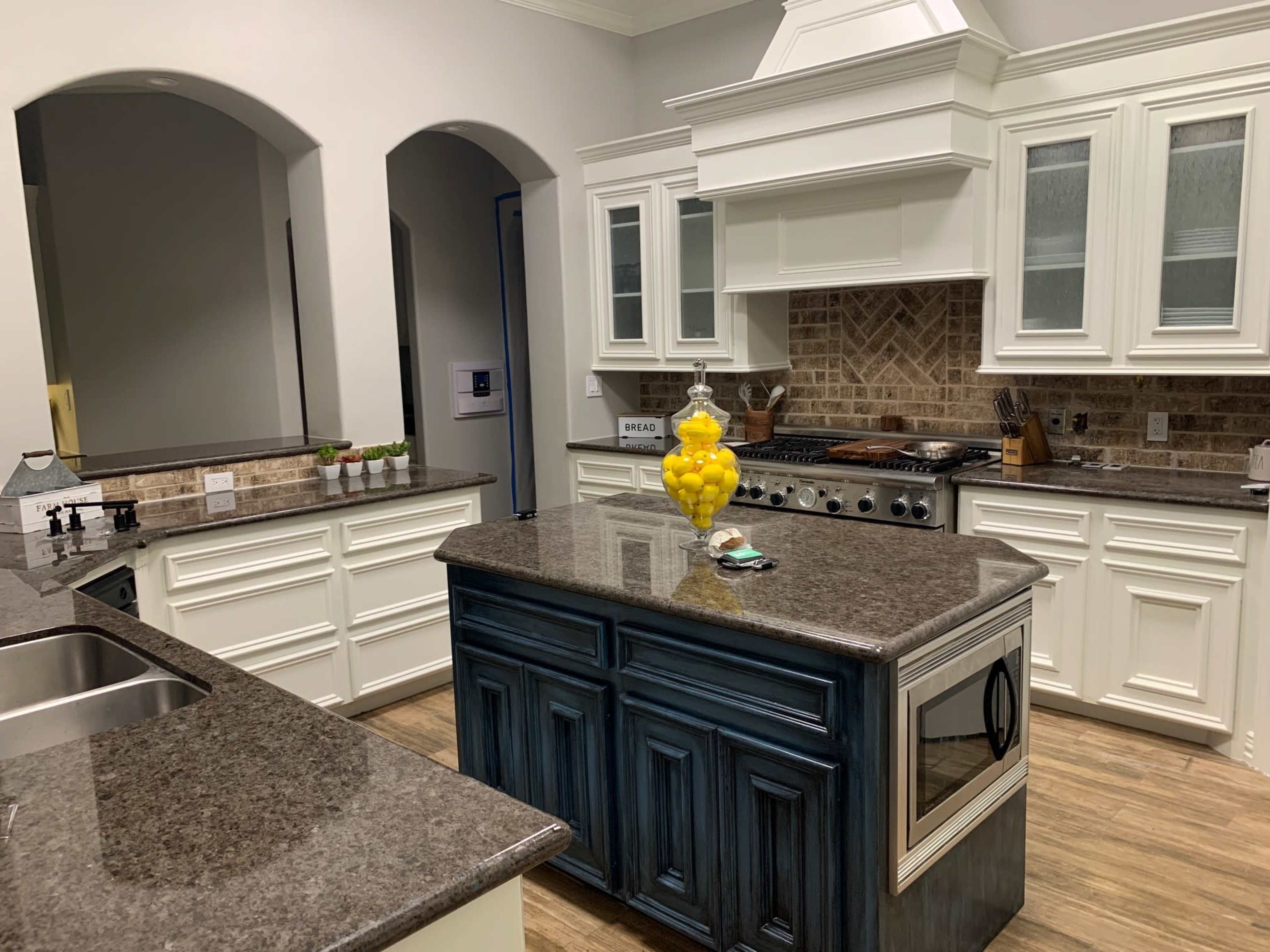 A modern kitchen with white cabinetry, a large dark countertop island, and a background of brick tiling.