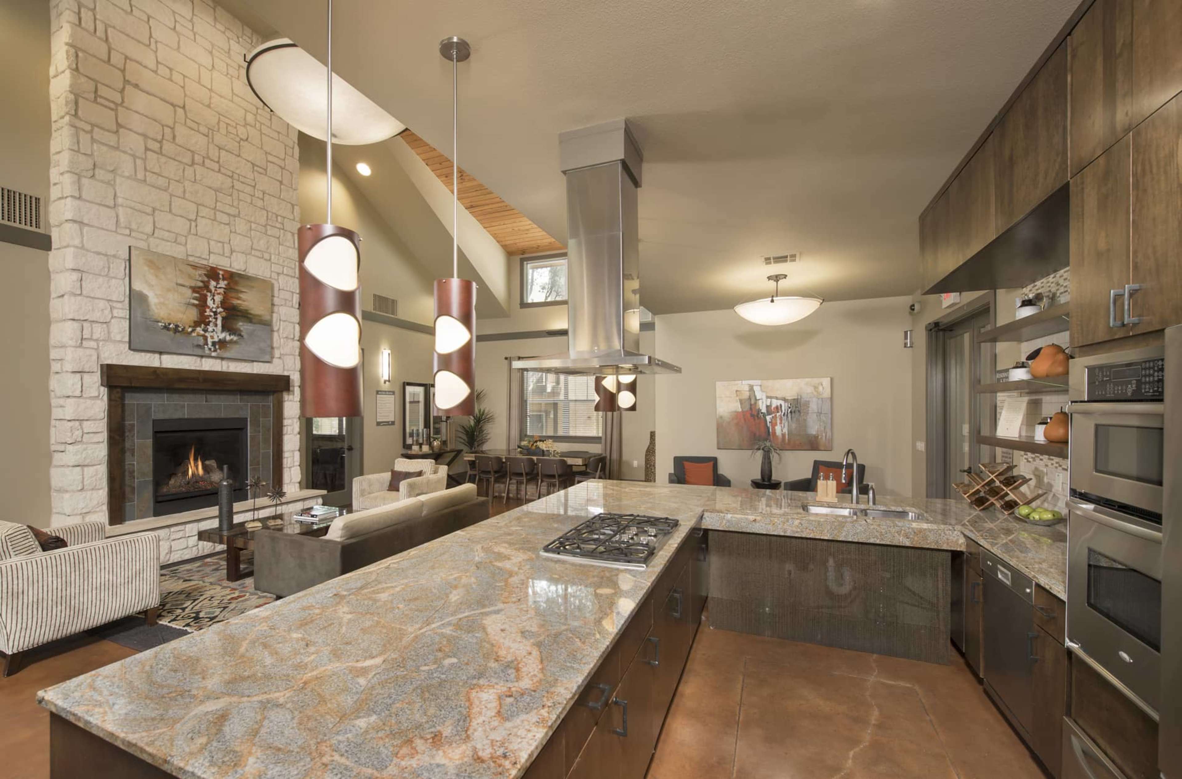 A modern kitchen connected to a living area, featuring a large island with a marble countertop, stainless steel appliances, and a stone fireplace in the background.