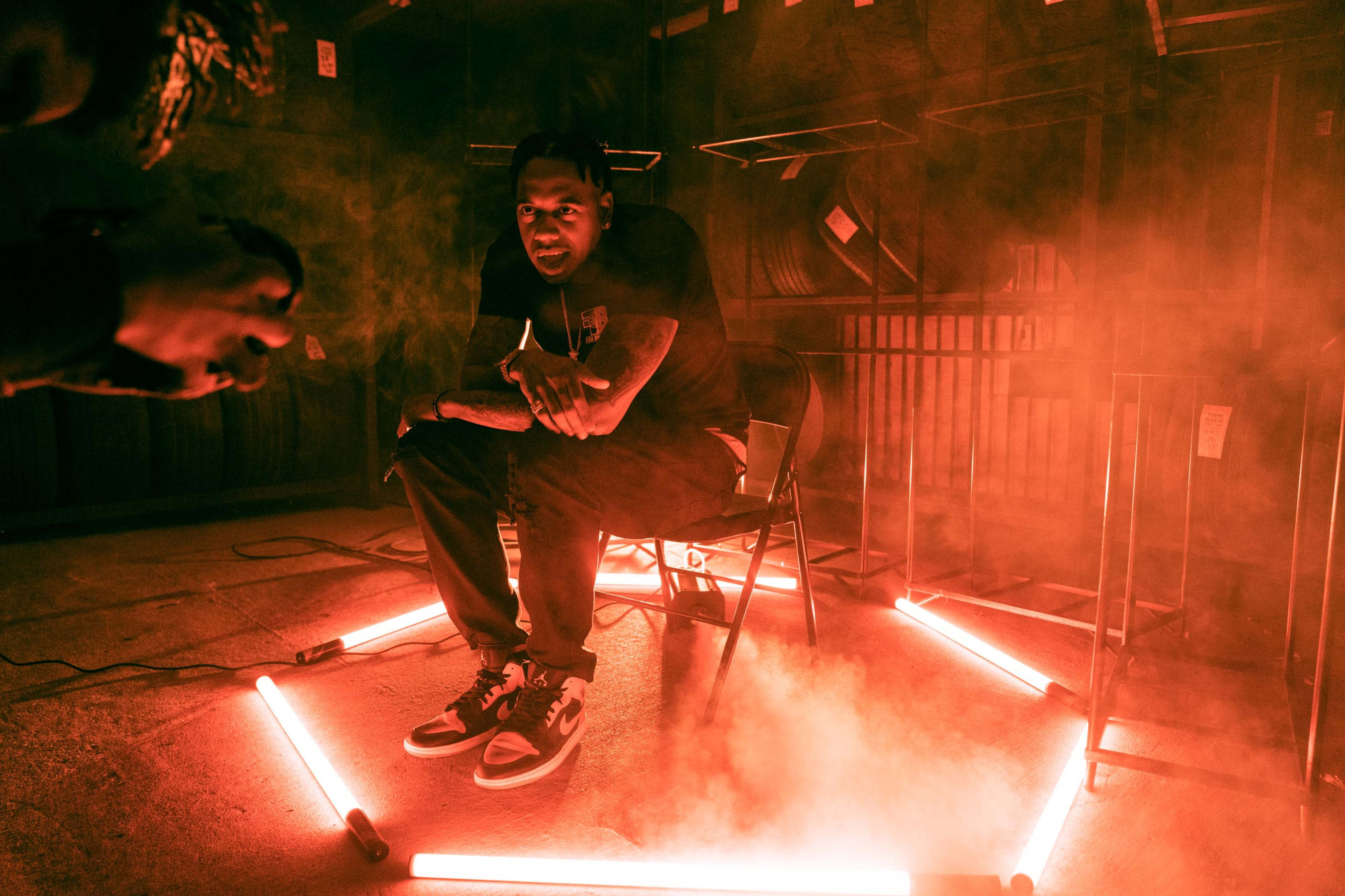 A person sits in a chair surrounded by glowing neon lights and mist in a dimly lit indoor space.