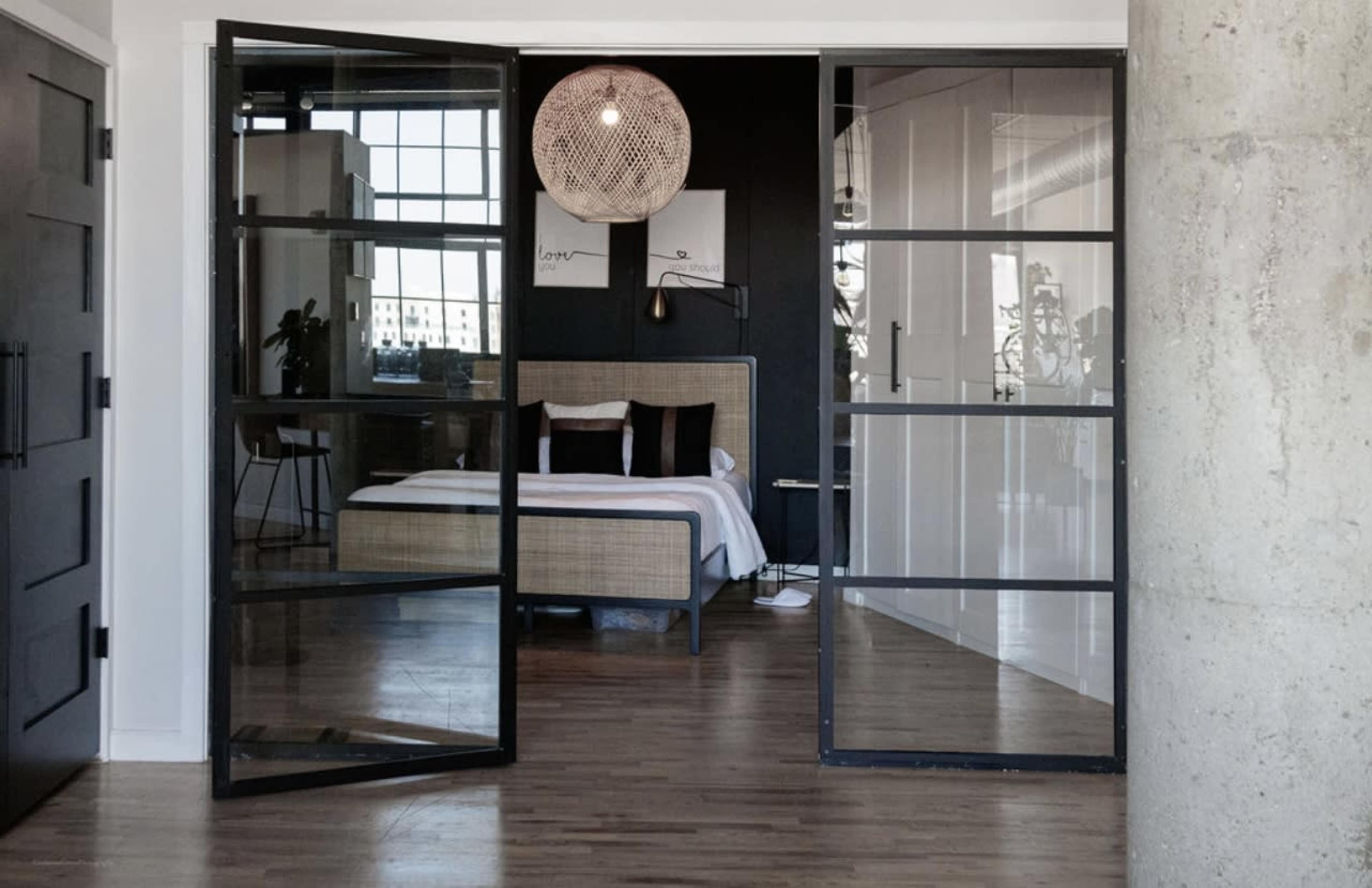 A modern bedroom with a queen-sized bed is visible through large glass doors in a stylish interior.